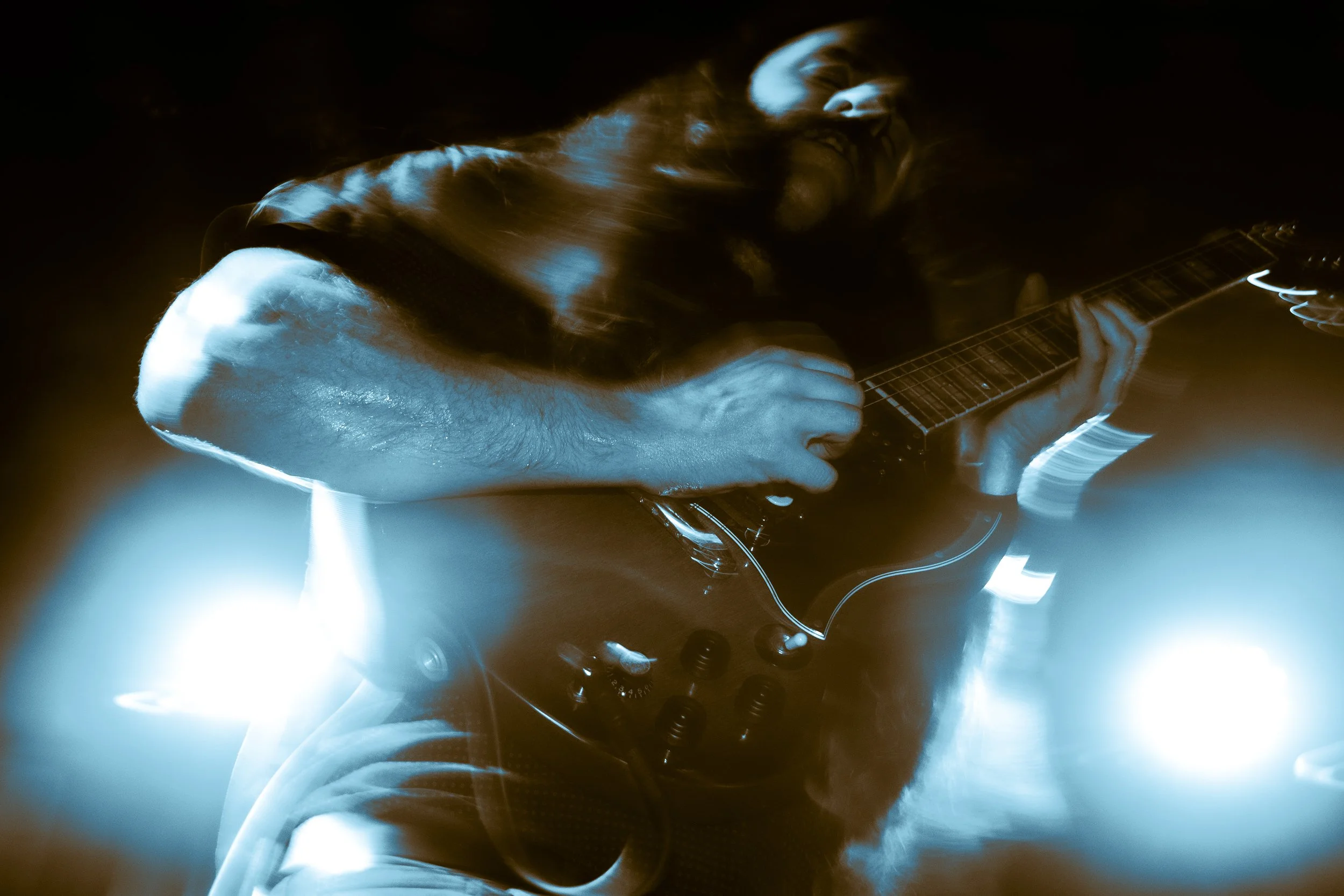 A person playing an electric guitar on stage with dynamic blue light effects.