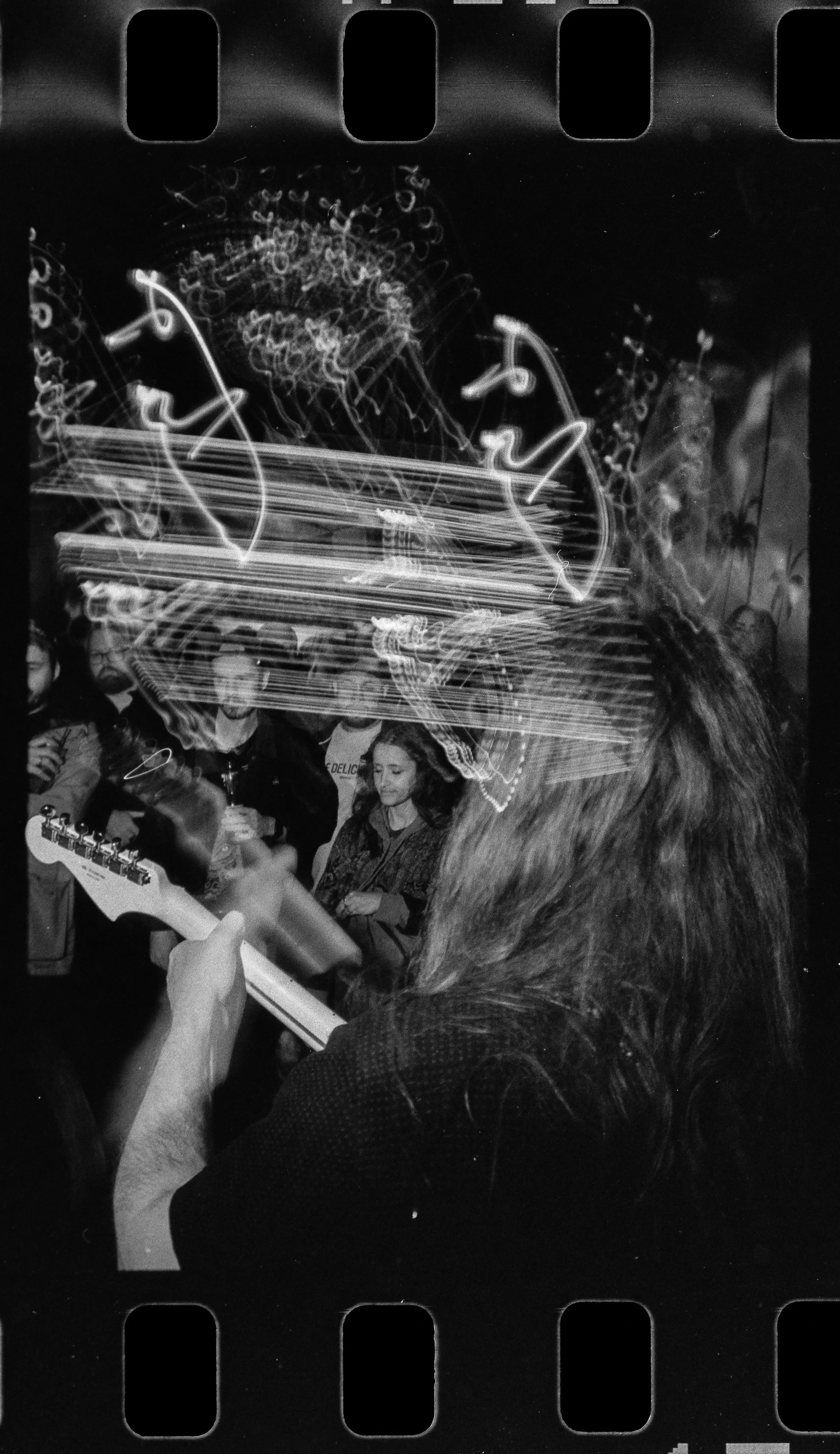Black and white photo of a group of people at a Liquid Pennies show at The Bends in Saint Petersburg Florida, with Chas Binns, Liquid Pennies bandleader playing guitar, at a live music event, with light trails and motion blur.