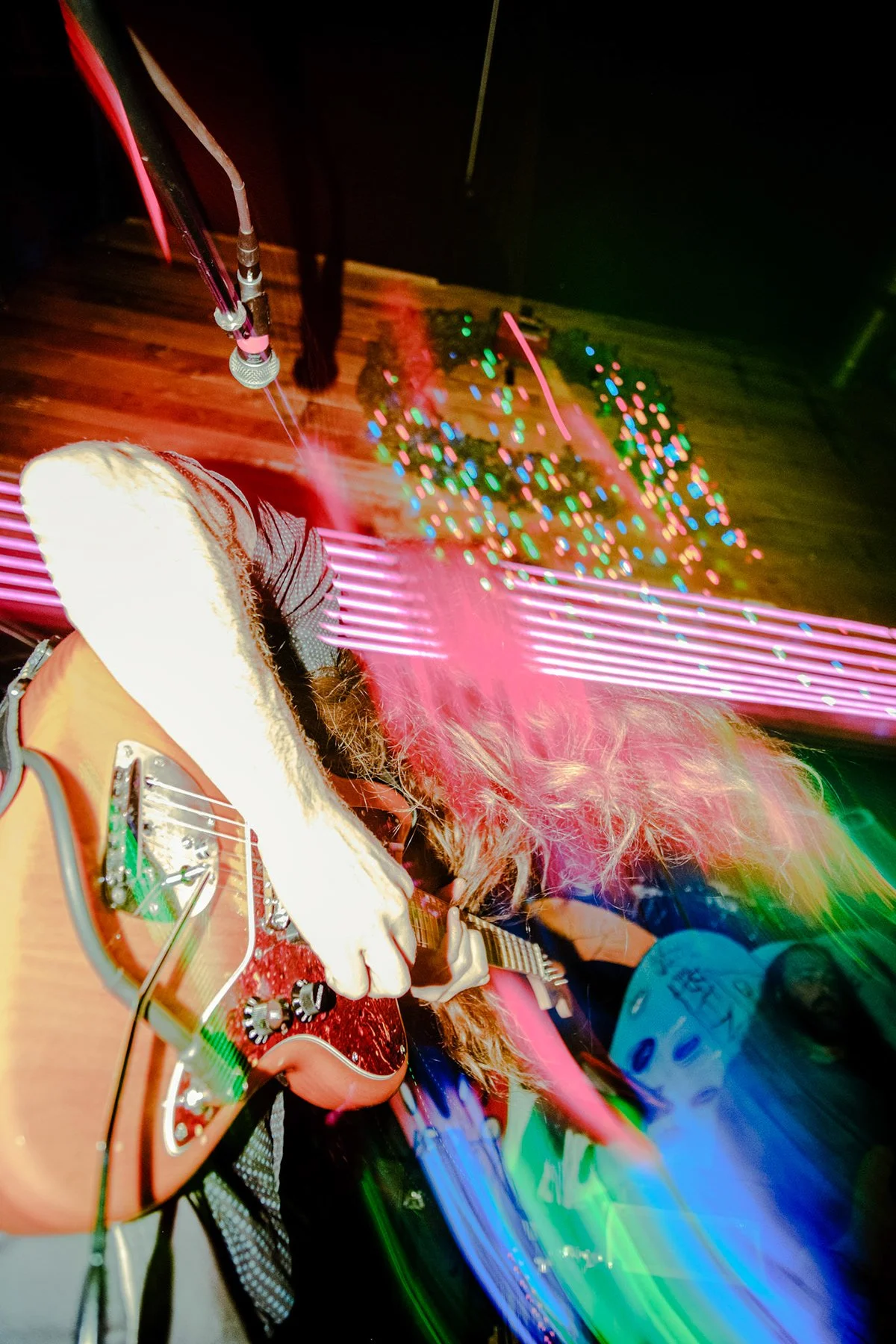 Person playing an acoustic guitar on stage with colored lights and motion blur.