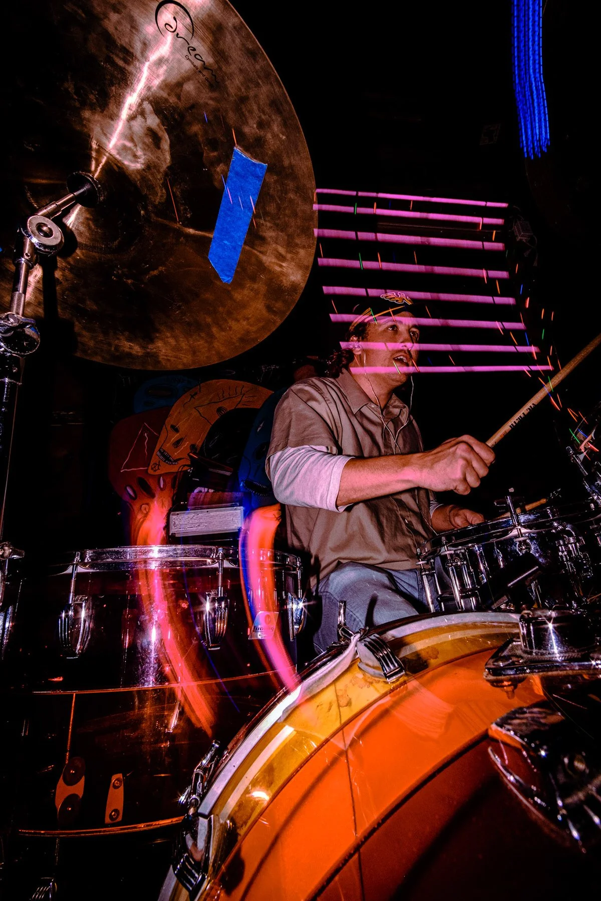 Liquid Pennies drummer Pierson Whicker playing a drum set on a stage with colorful lights and long exposure motion effects.