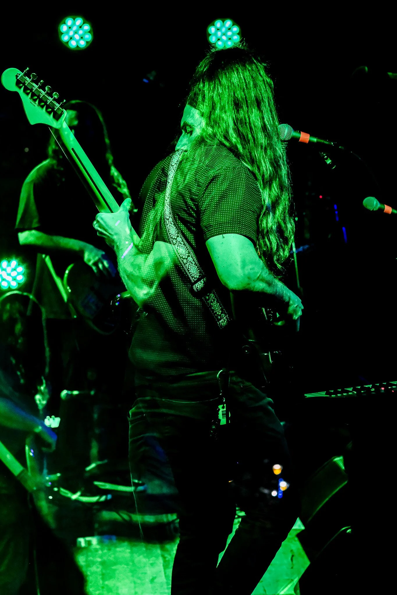Musician playing electric guitar on stage under green lighting.