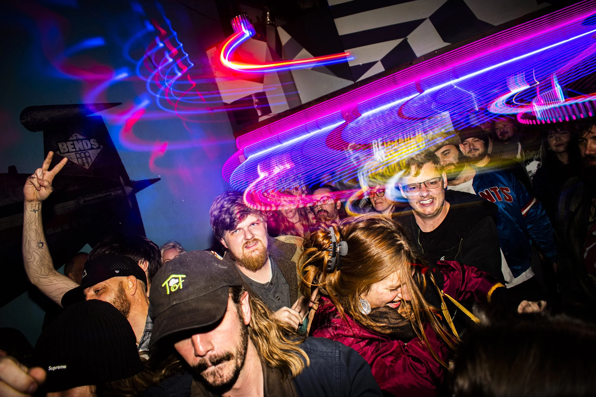 Group of people dancing and having fun at a party with colorful light streaks in the background.