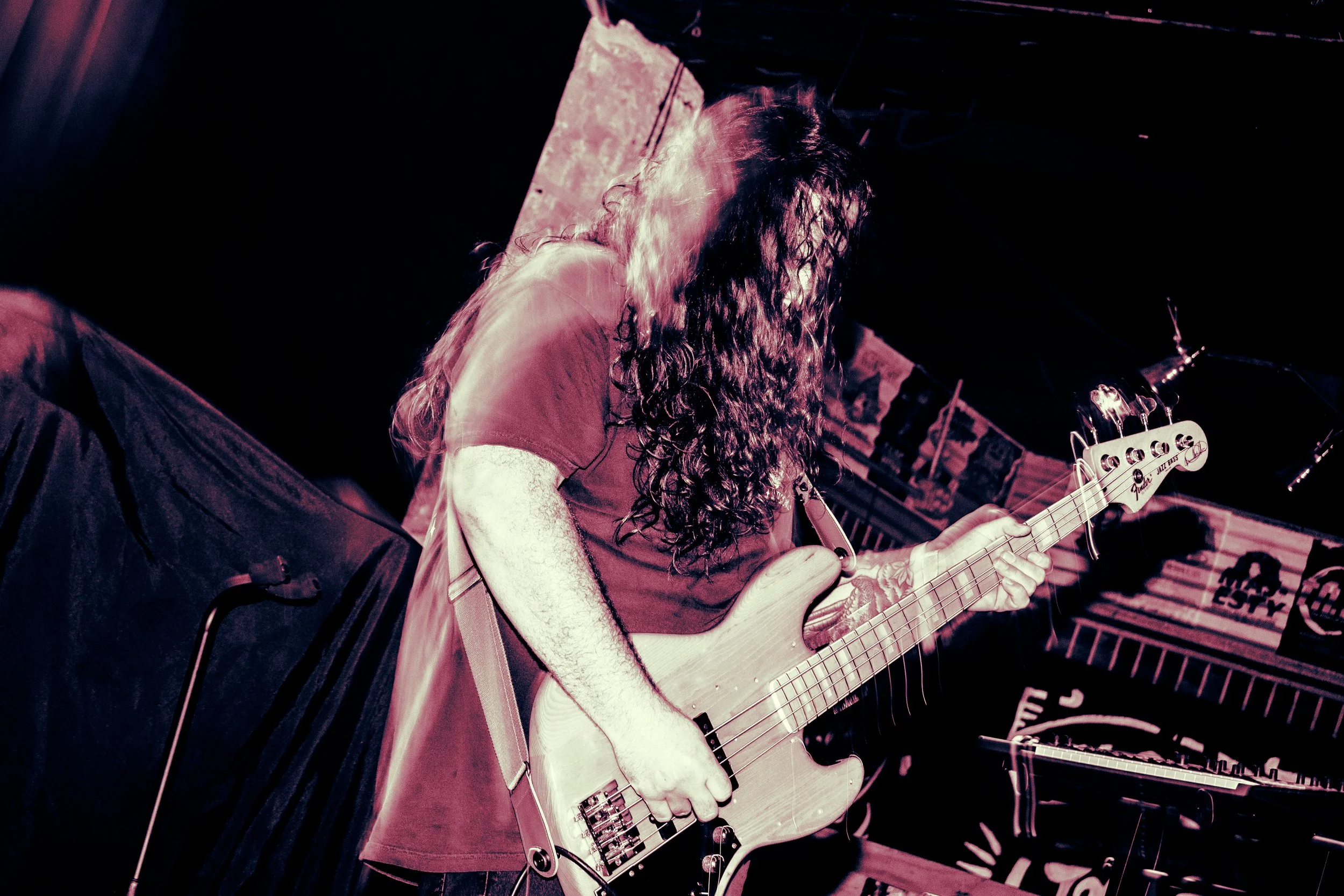 Musician with long curly hair playing an electric bass guitar on stage at a live concert.