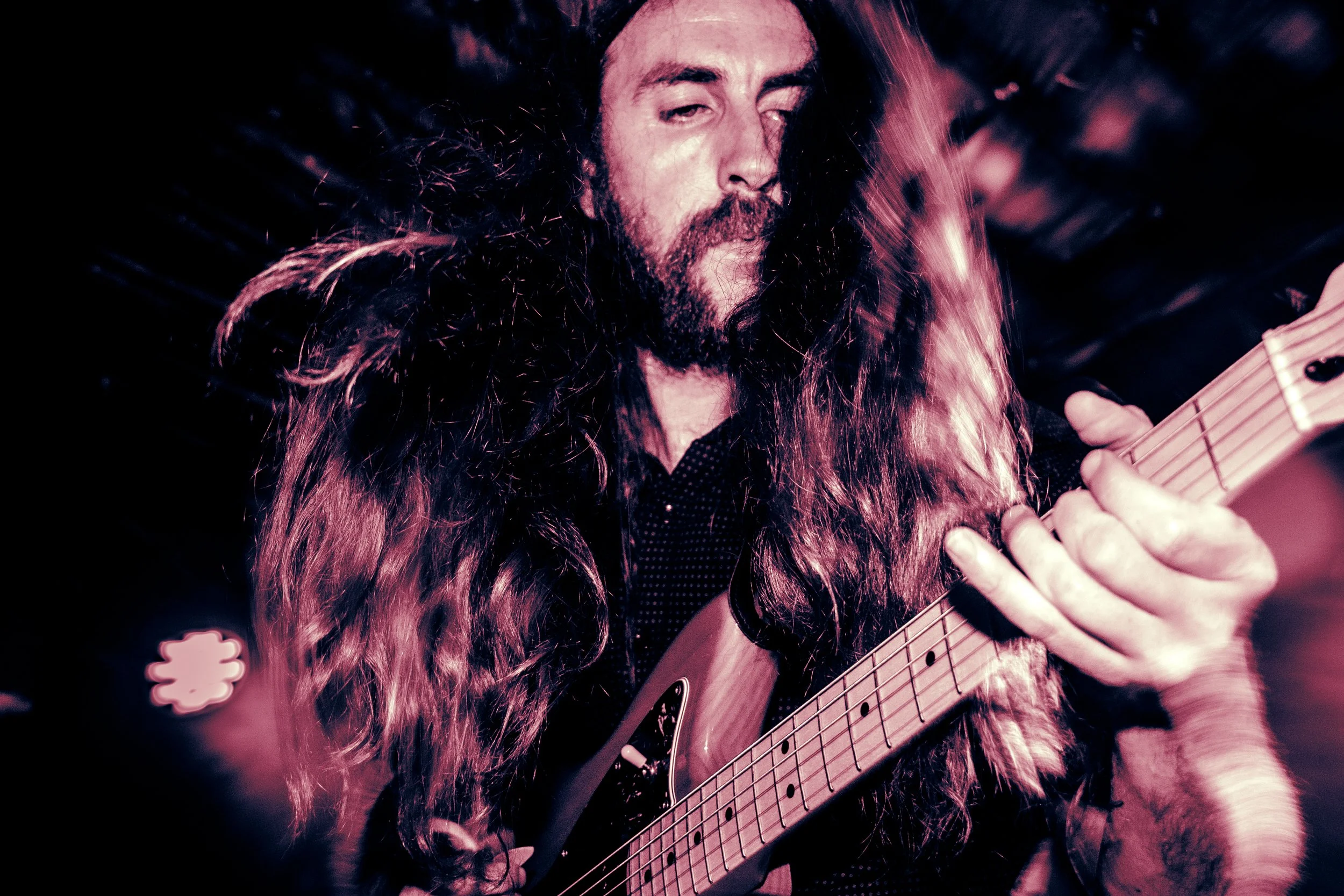 Rock band Liquid Pennies frontman/guitarist Chas BInns playing electric guitar during one of their kinetic psych-rock concerts.
