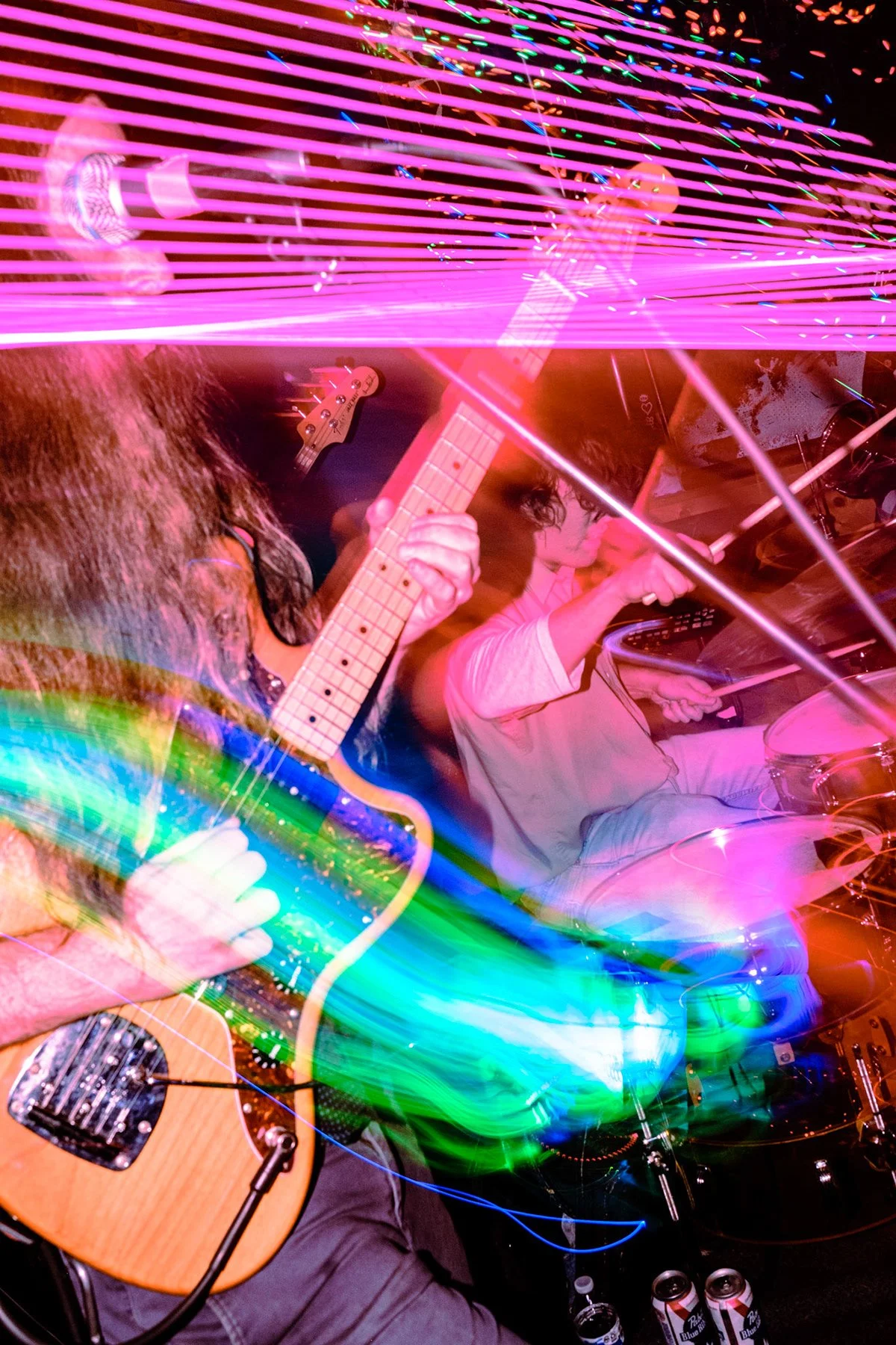 Musicians performing with neon and colorful light effects, one playing guitar and another on drums, in a lively concert or jam session.