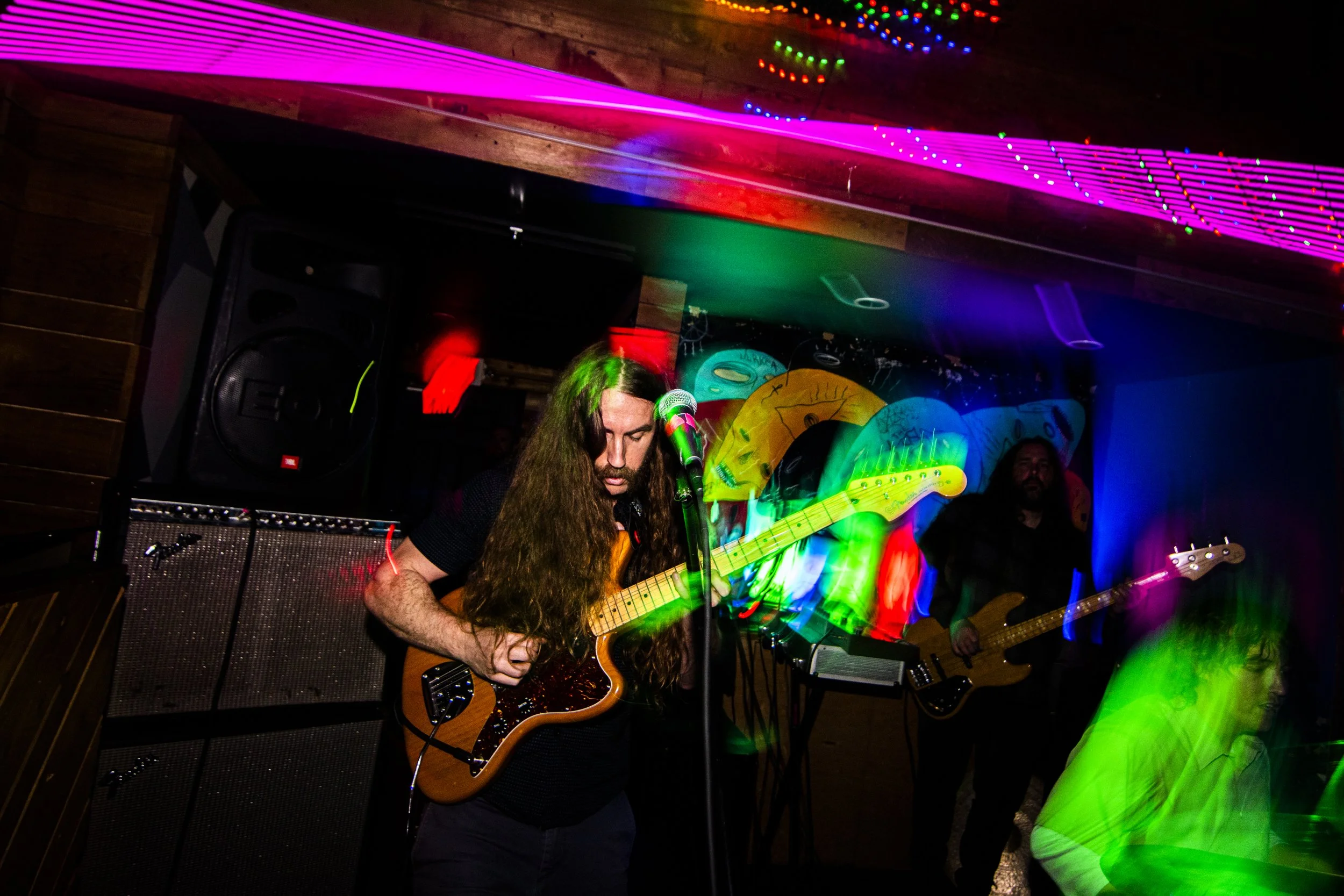 Musicians performing on stage with colorful lights and a backdrop featuring cartoon faces.