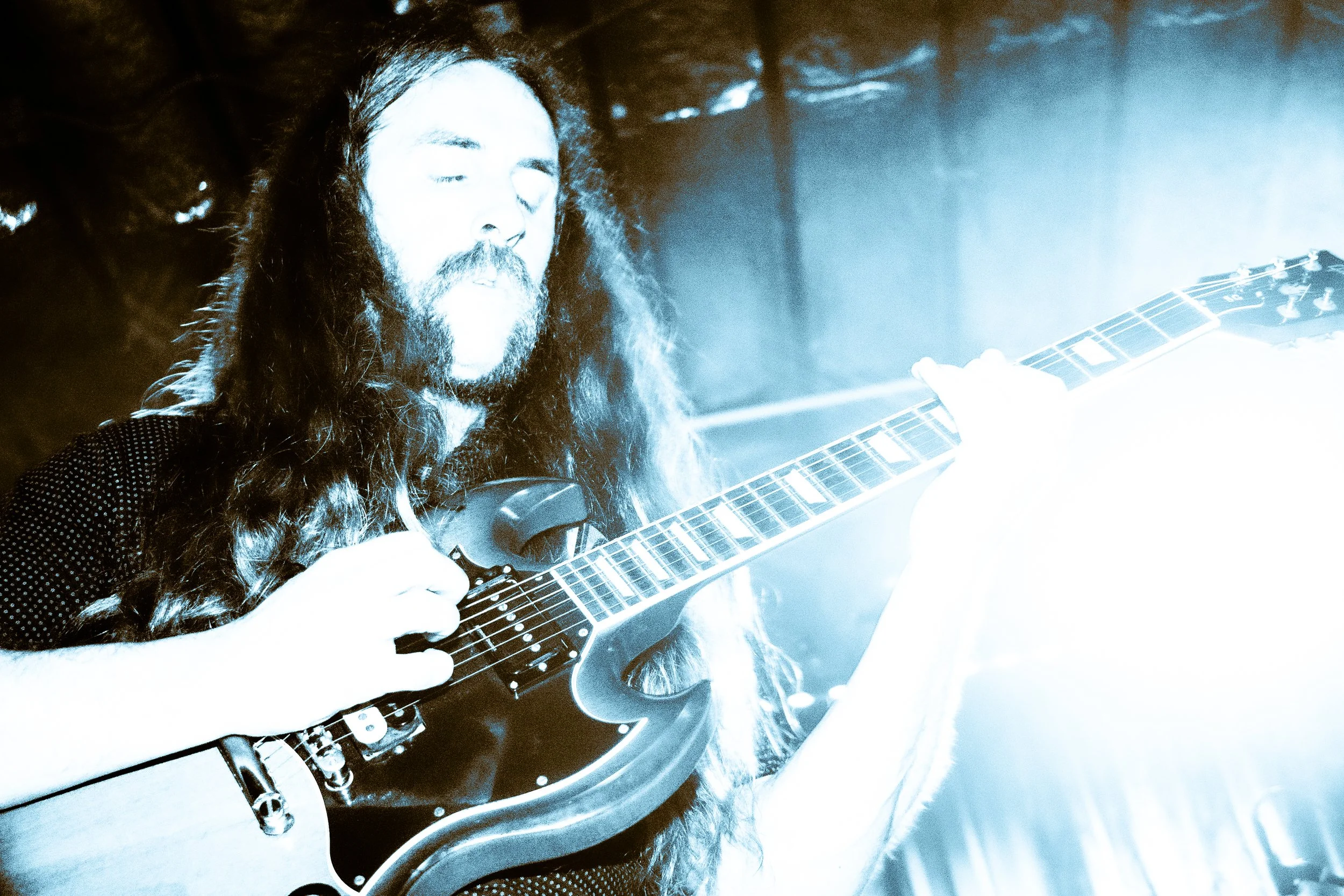 Chas Binns of Liquid Pennies playing an electric guitar on stage, with bright lighting and a smoky background at Crowbar in Ybor city
