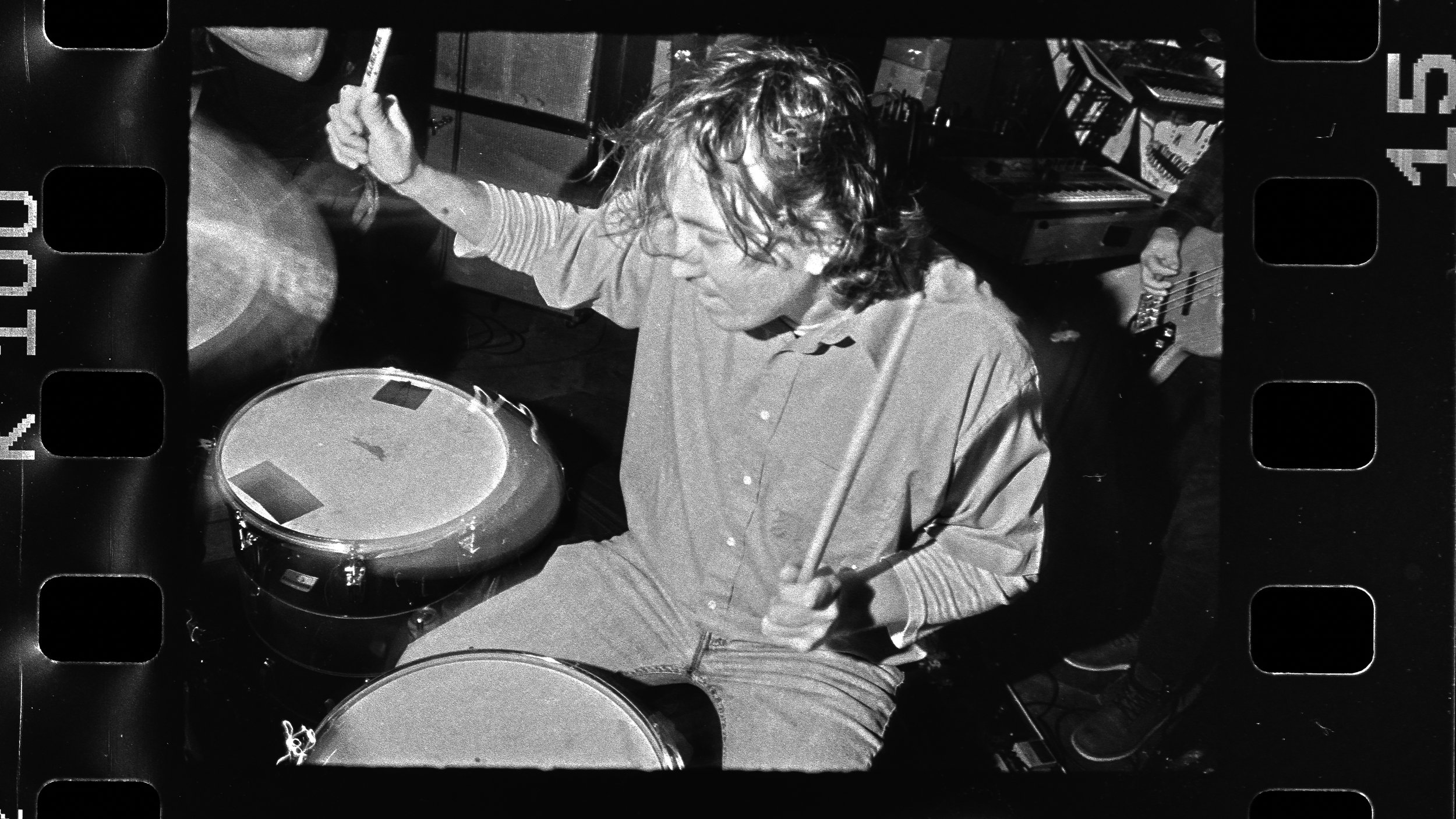 A person with curly hair playing drums in a recording studio.