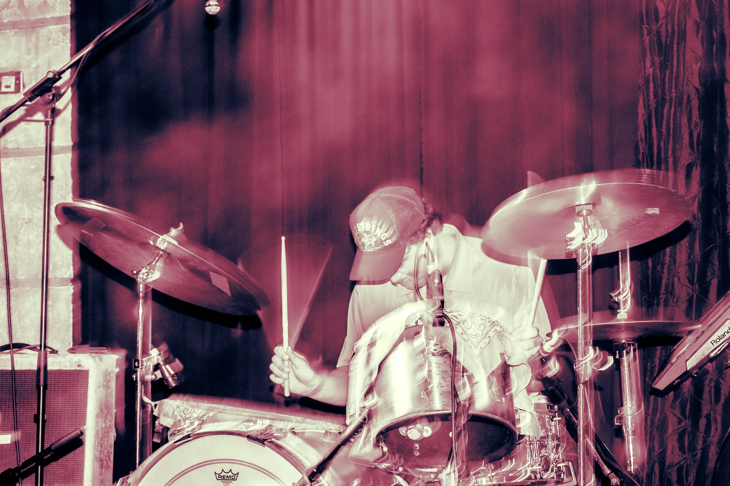 Psych rock band Liquid Pennies drummer PIerson Whicker  wearing a baseball cap and headphones playing a drum set on stage.