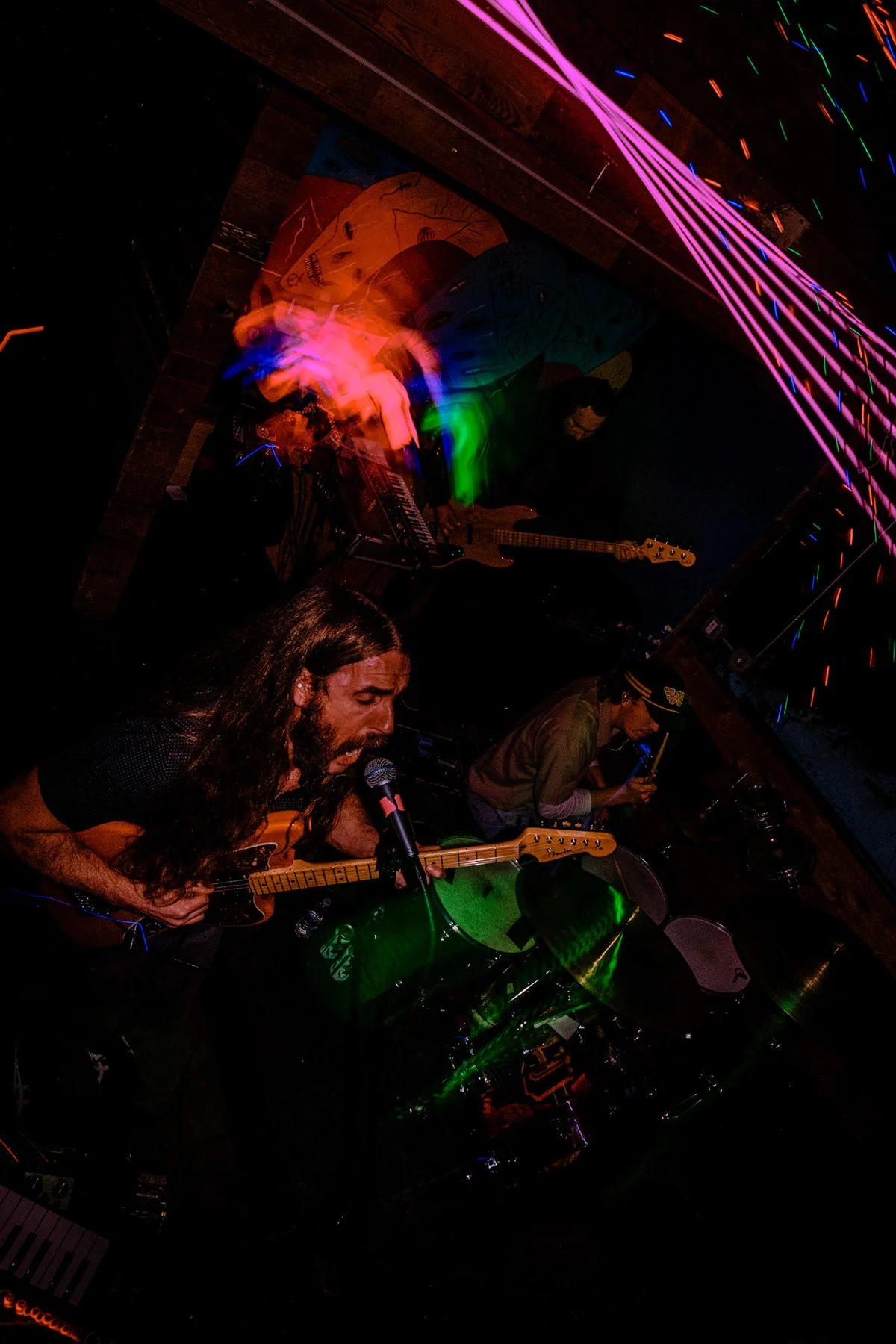 Liquid Pennies perform with colorful neon lights and abstract artwork on the wall.