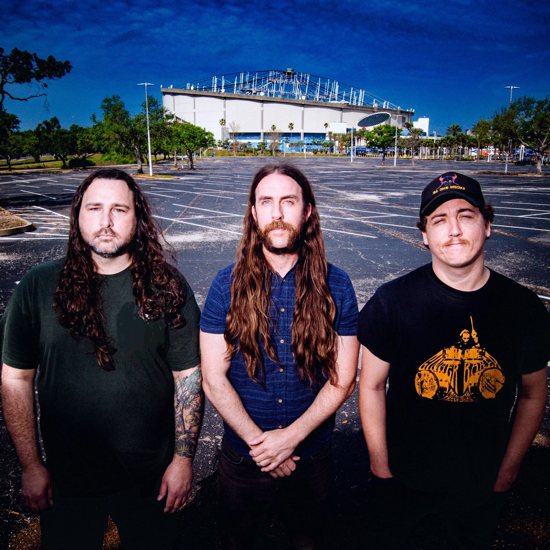 Liquid Pennies offical press photo in 2025. Left to right: Tysonious Mink (bass/synthesizer), Chas Binns (guitar/vocals/synth/keys), and Pierson Whicker (drums). Taken in front of the damaged Tropicana Field in St Petersburg, Florida. Psych rock band
