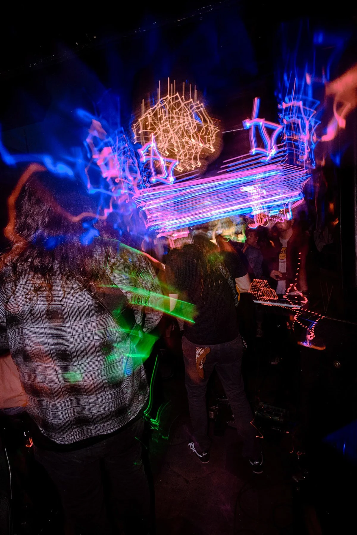 People dancing and socializing in a nightclub with colorful neon light streaks and abstract light patterns.