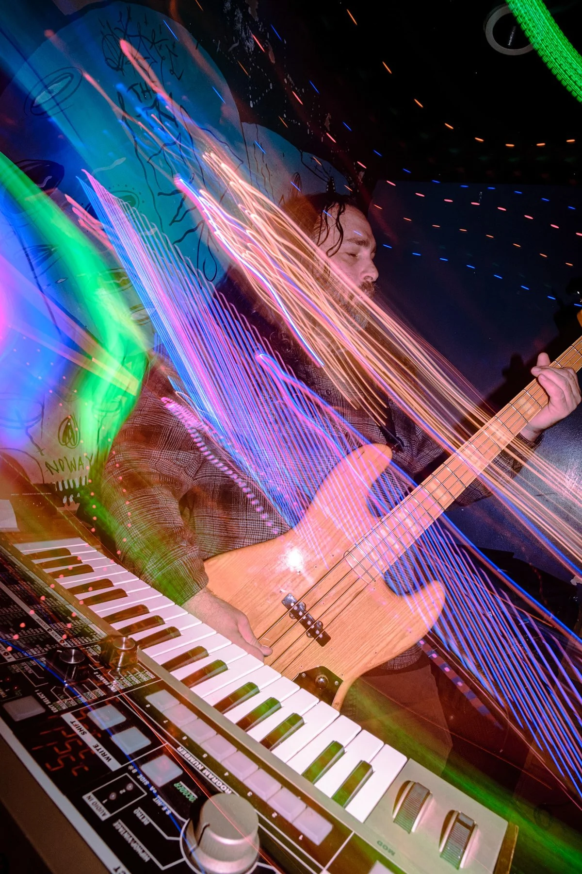 A musician playing an electric bass guitar and synthesizer, with colorful light trails creating a dynamic, vibrant scene.
