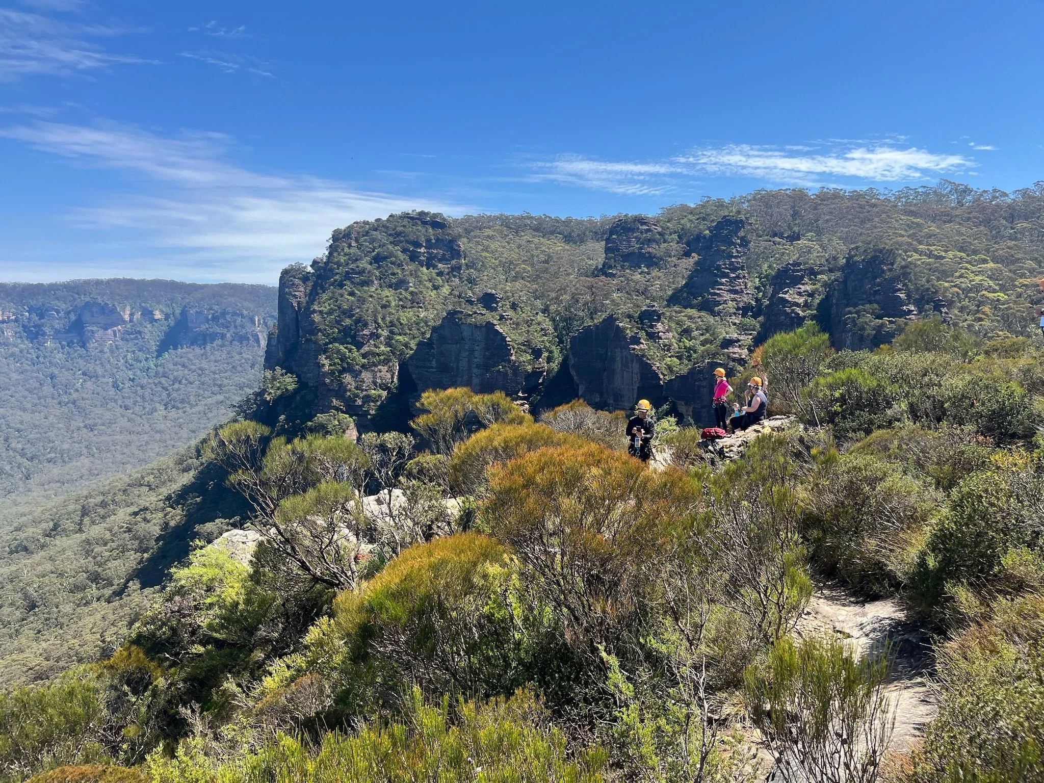 Participants in a leadership development program experience the unique 'Eek & Awe' method from Out Of Bounds on a mountain cliff edge, surrounded by dramatic canyon formations and native bushland in Australia.
