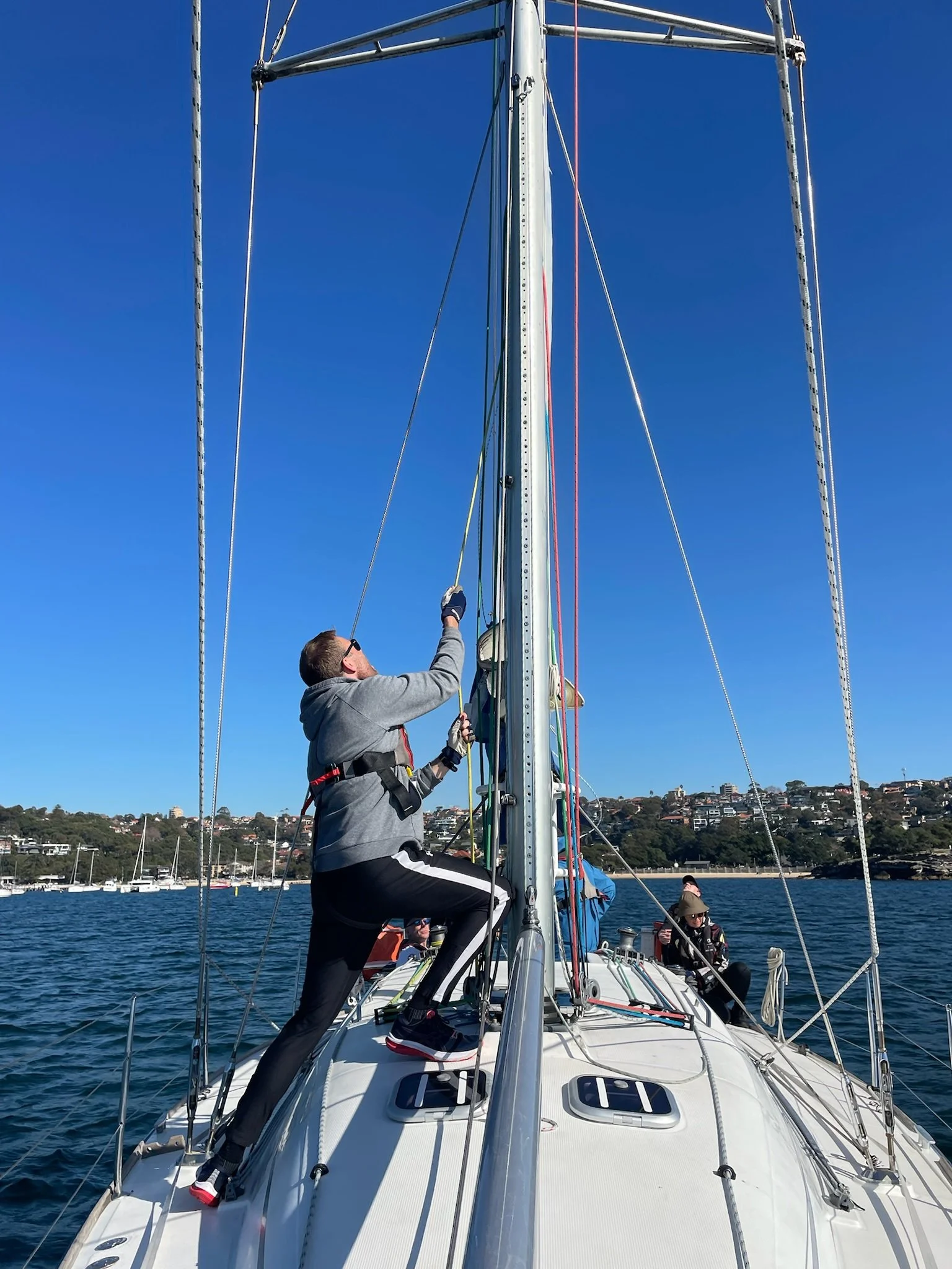 A participant climbs the mast of a sailboat during a leadership development program experience in Australia while another team member watches from the deck.