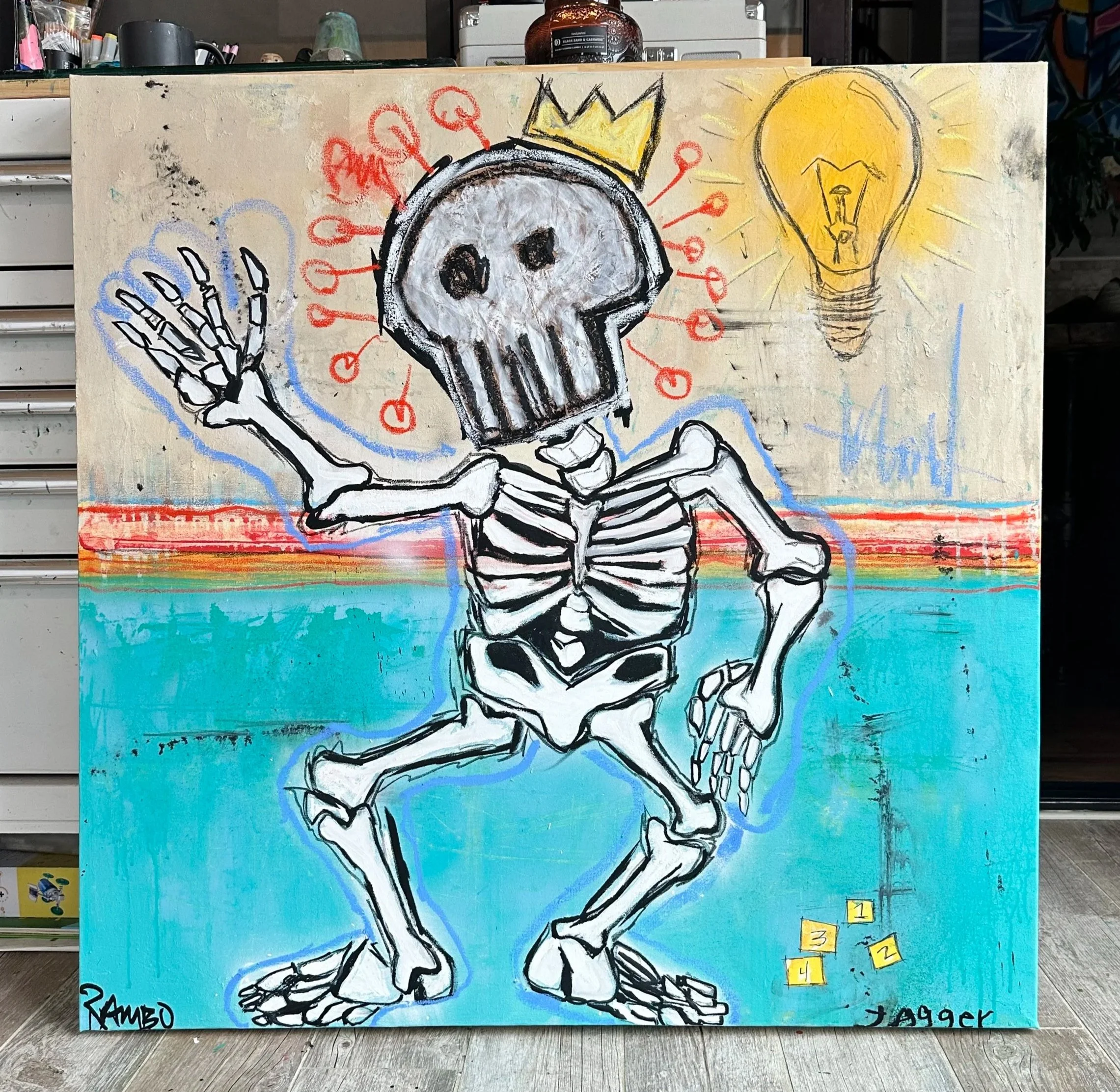 Street art of a skeleton with a crown, holding a blue heart, with a yellow light bulb symbol above its head, on a colorful background.