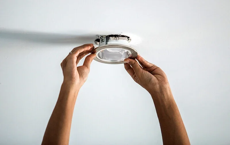 Person installing or replacing a ceiling light fixture in a white ceiling.