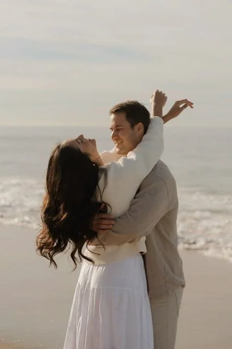 A couple embracing and smiling on the beach, with the ocean in the background.