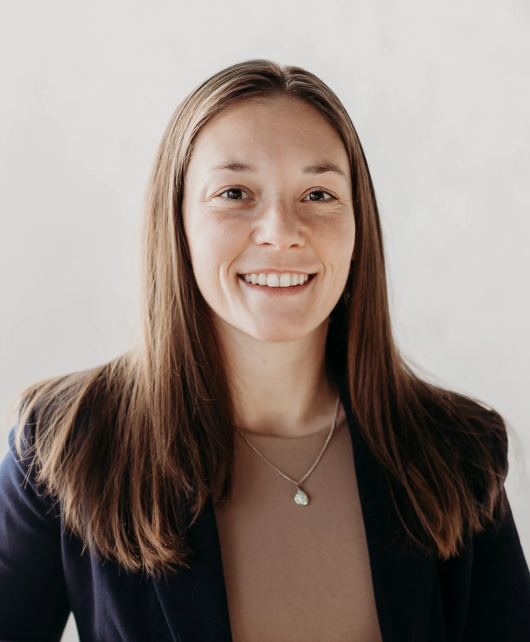 Portrait of a smiling woman with brown hair wearing a dark blazer and a necklace