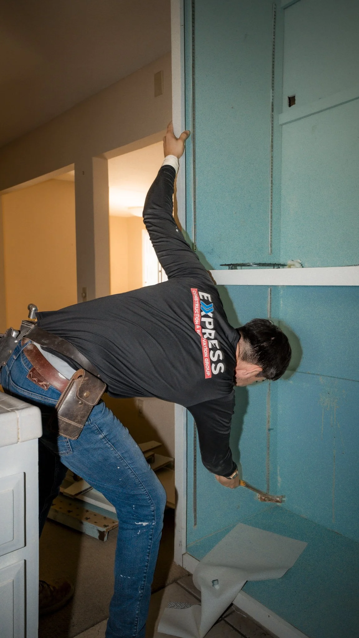 A man installing blue drywall in a home, using a hammer to secure it to the wall.