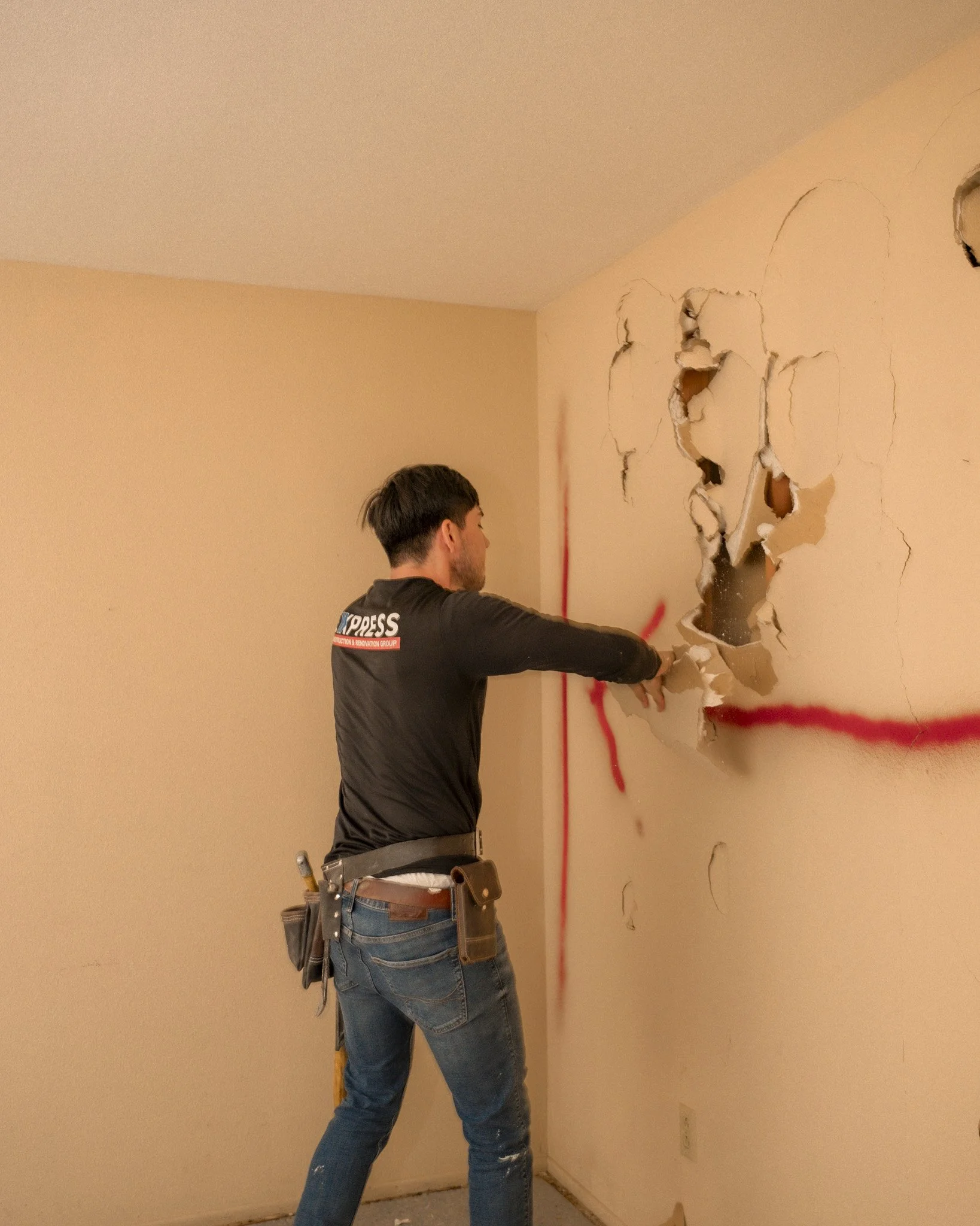A man breaking through a damaged wall with a punch, revealing holes and cracks, in an indoor setting.