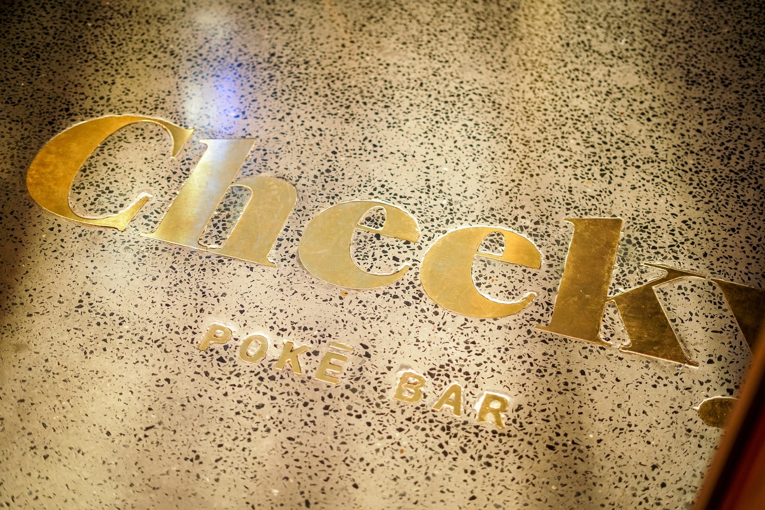 Close-up of a textured gold surface with the words 'Chick' and 'Poke Bar' in raised gold lettering.