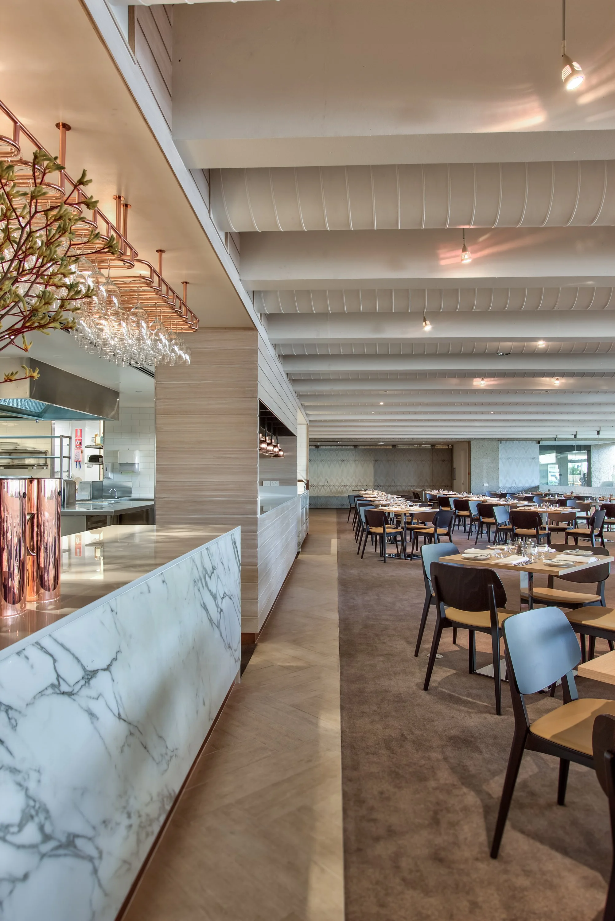 Interior of a modern restaurant with a marble counter, wooden tables and chairs, and a ceiling with exposed beams and spotlights.