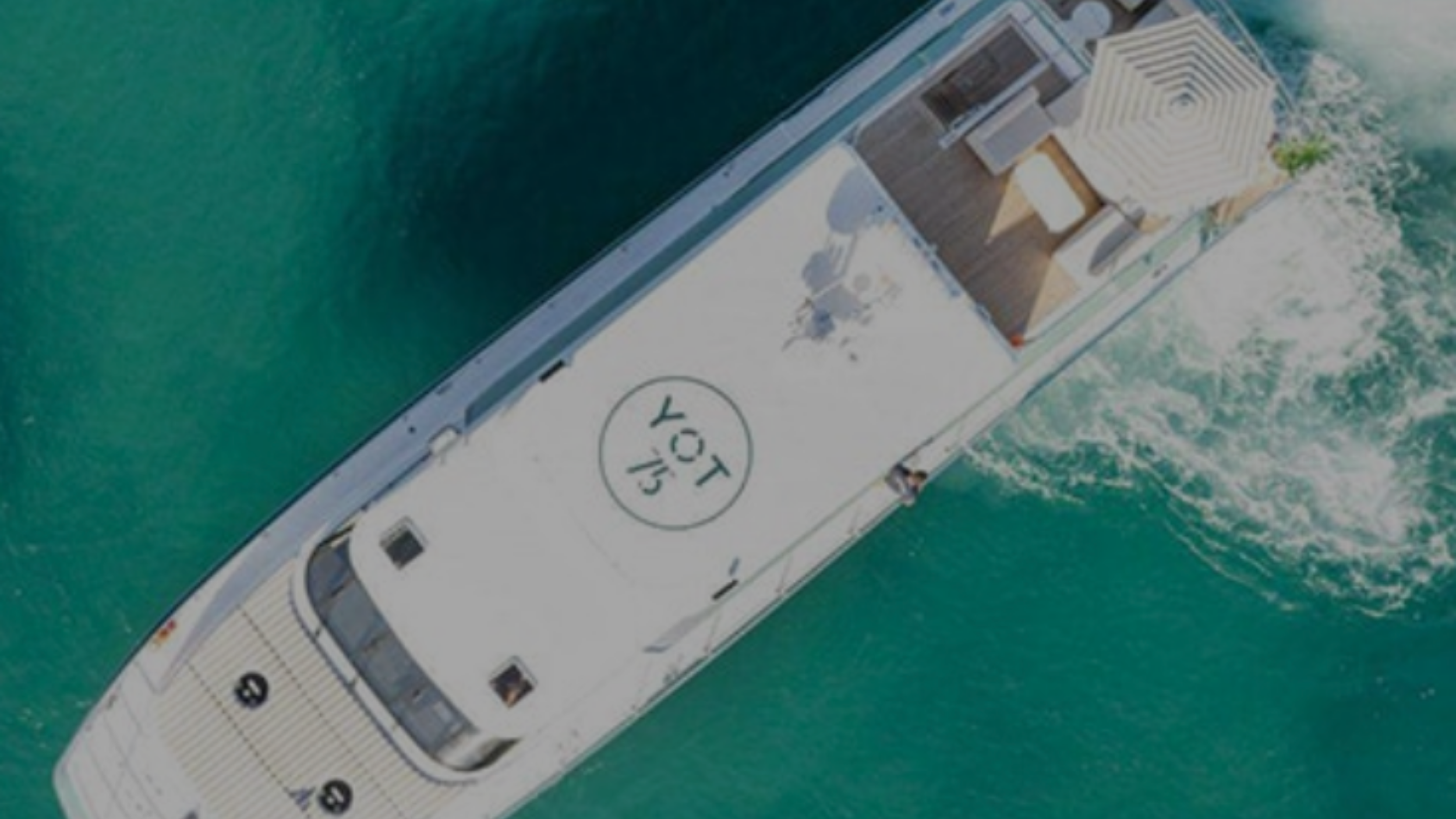 Aerial view of a boat on turquoise water with a rooftop helipad marked 'LOVE YOU' and a shaded lounge area at the stern.