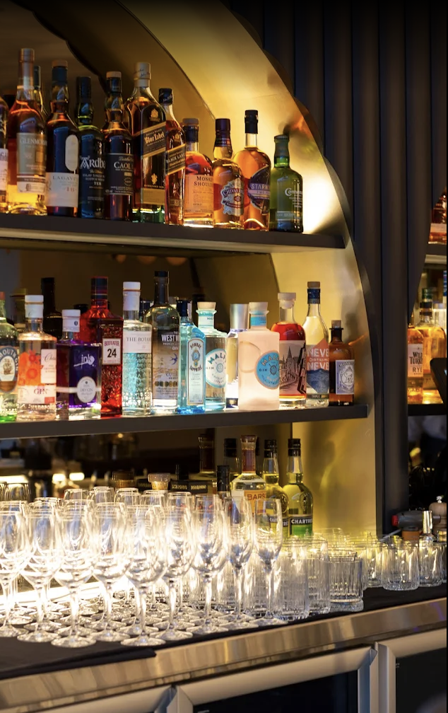 Bar shelf with various liquor bottles and rows of empty glasses.