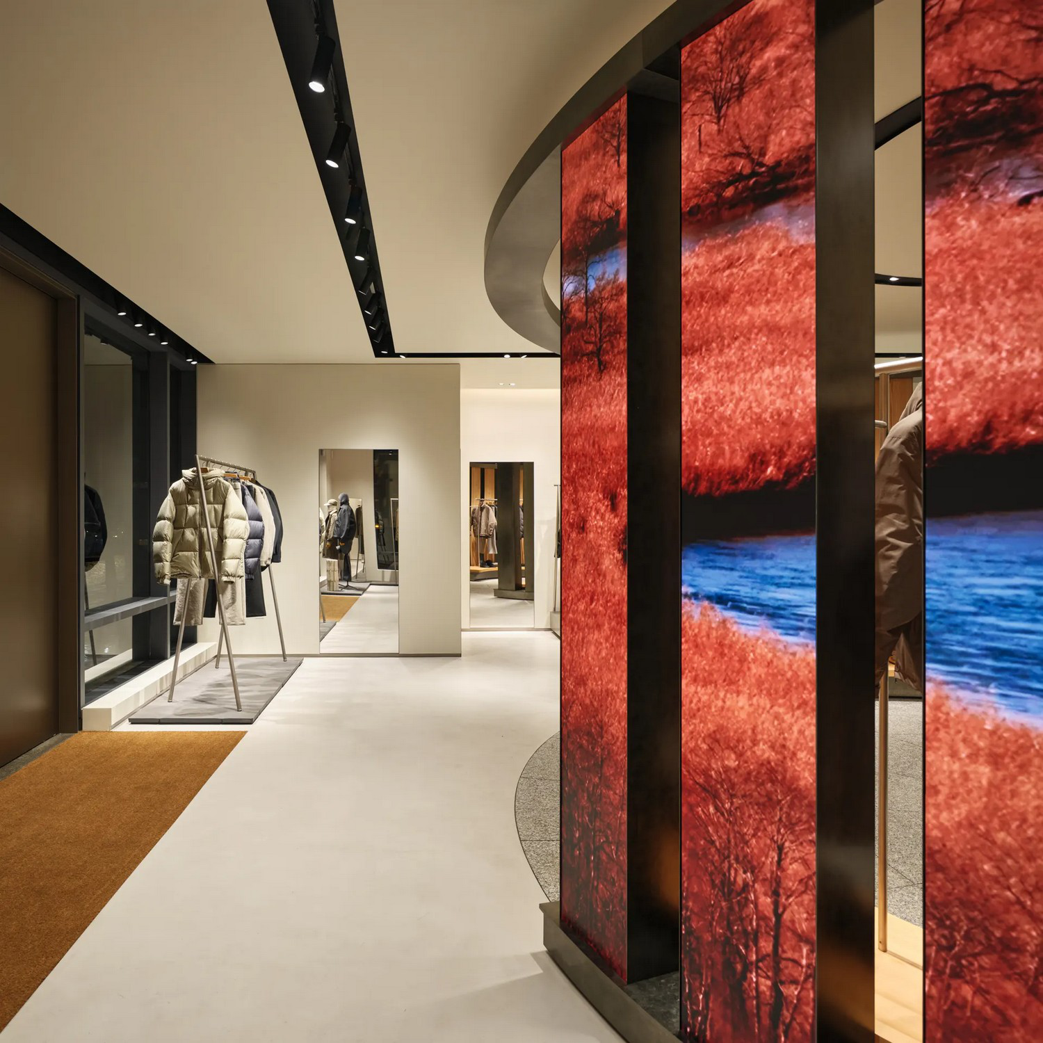 Red and blue moving imagery on digital columns beside clothing displays in Goldwin London.
