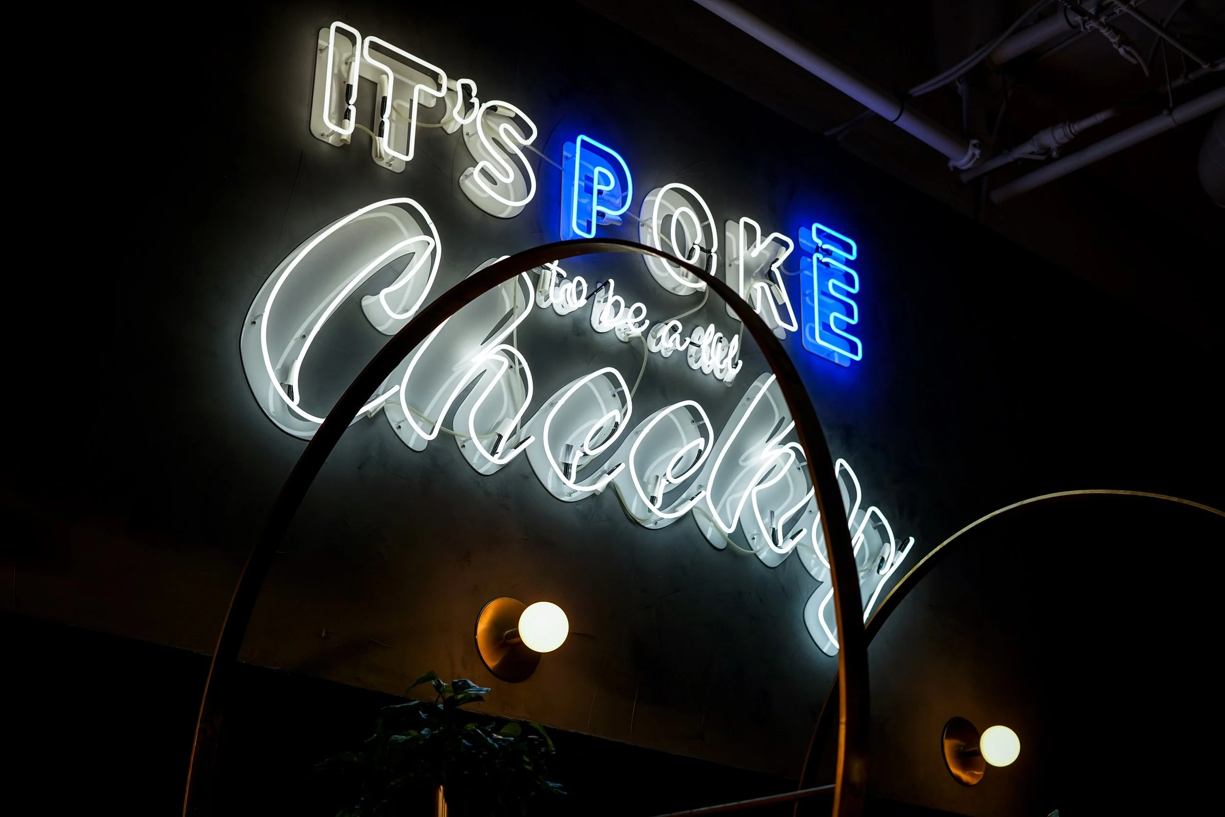 Neon sign with the words "It's Cookie" and "Still be a doll" in a dark room, with a curved metal frame and wall sconces visible.