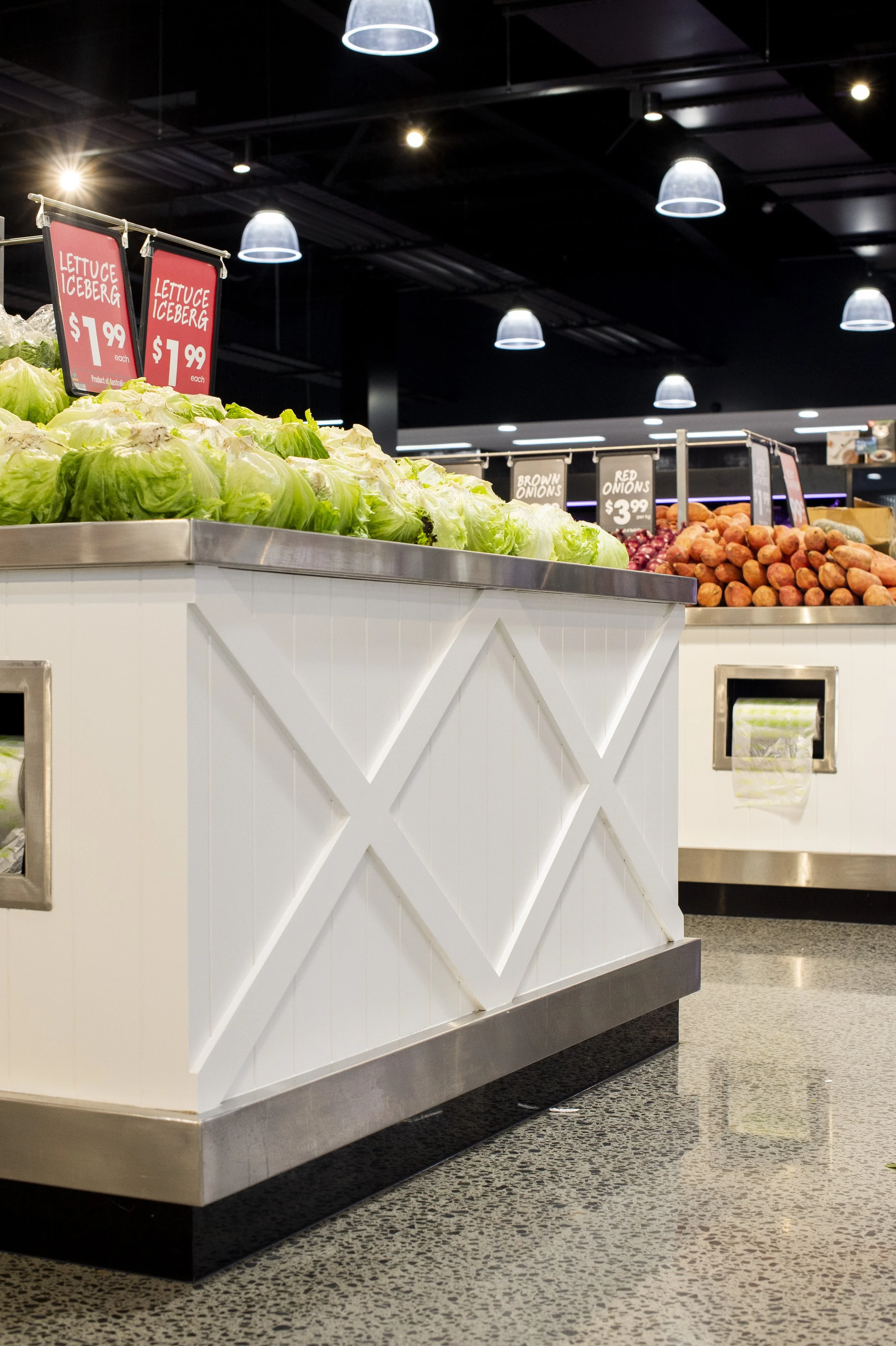Fresh lettuce heads and other vegetables on display at a grocery store produce section.