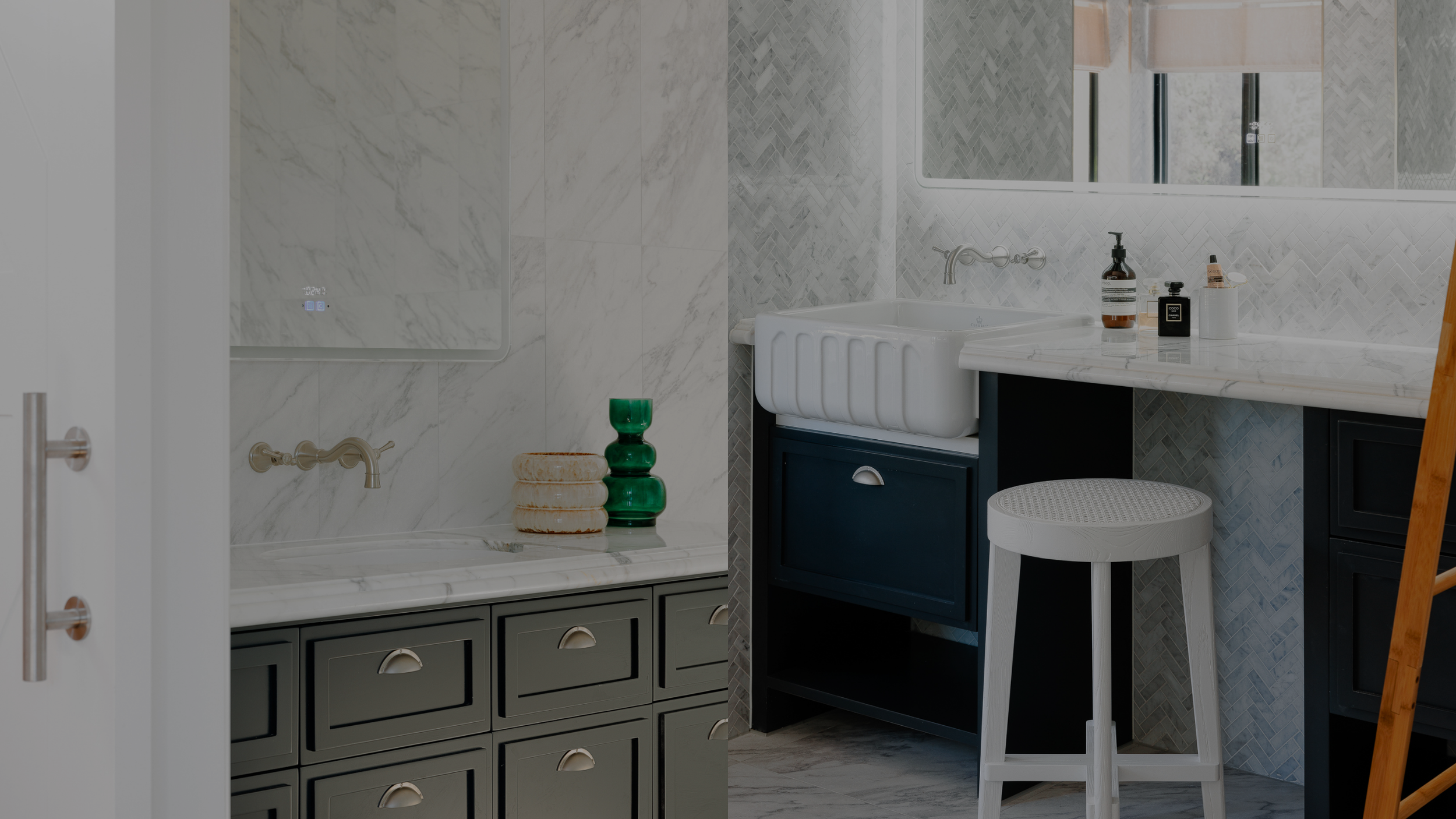 A bathroom with marble walls, a white basin, dark blue cabinet, wooden ladder, and gray cabinet with decorative items on the countertop.