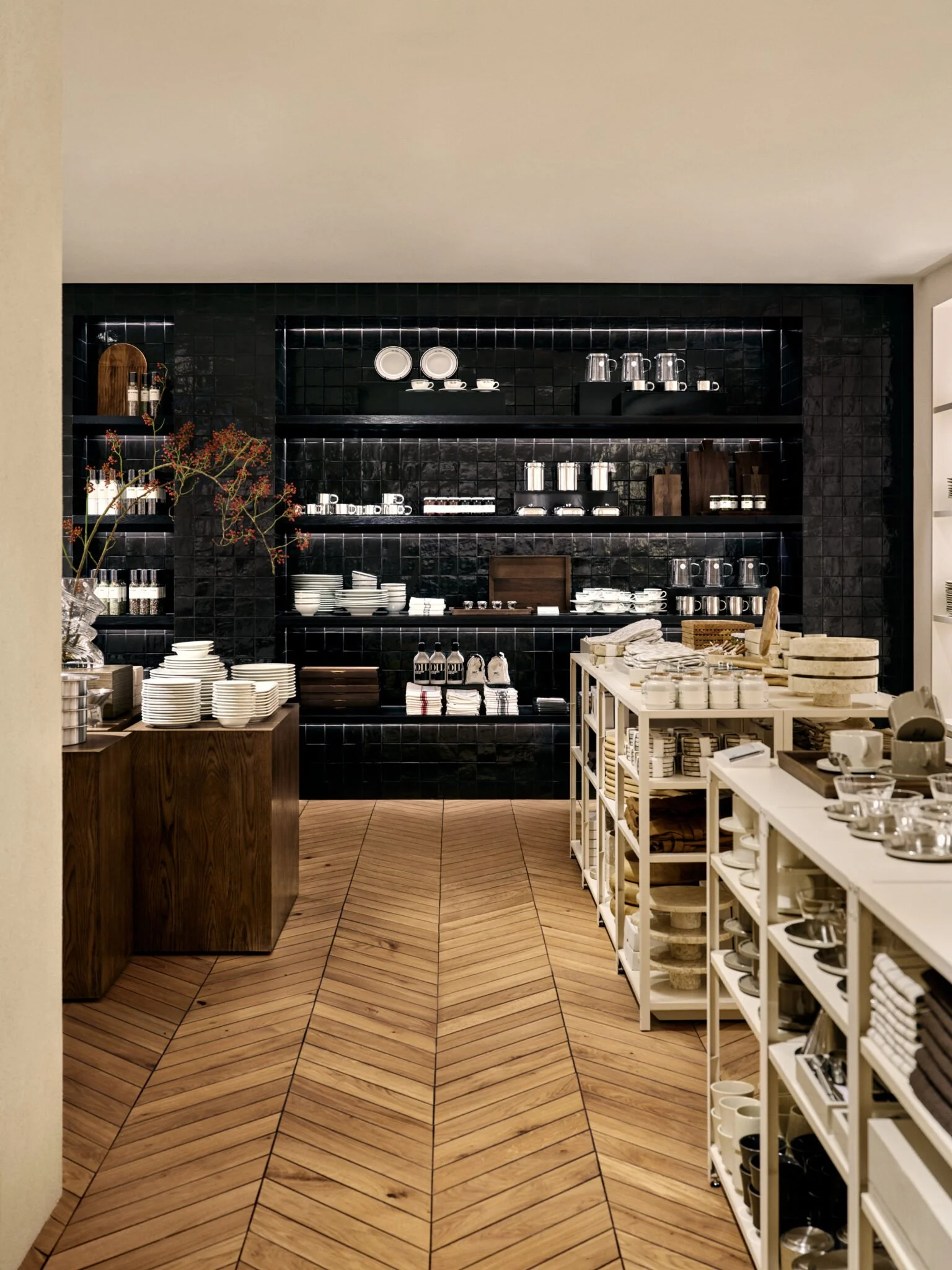 Dark tiled display wall, timber joinery and herringbone flooring at H&M Home Stockholm.