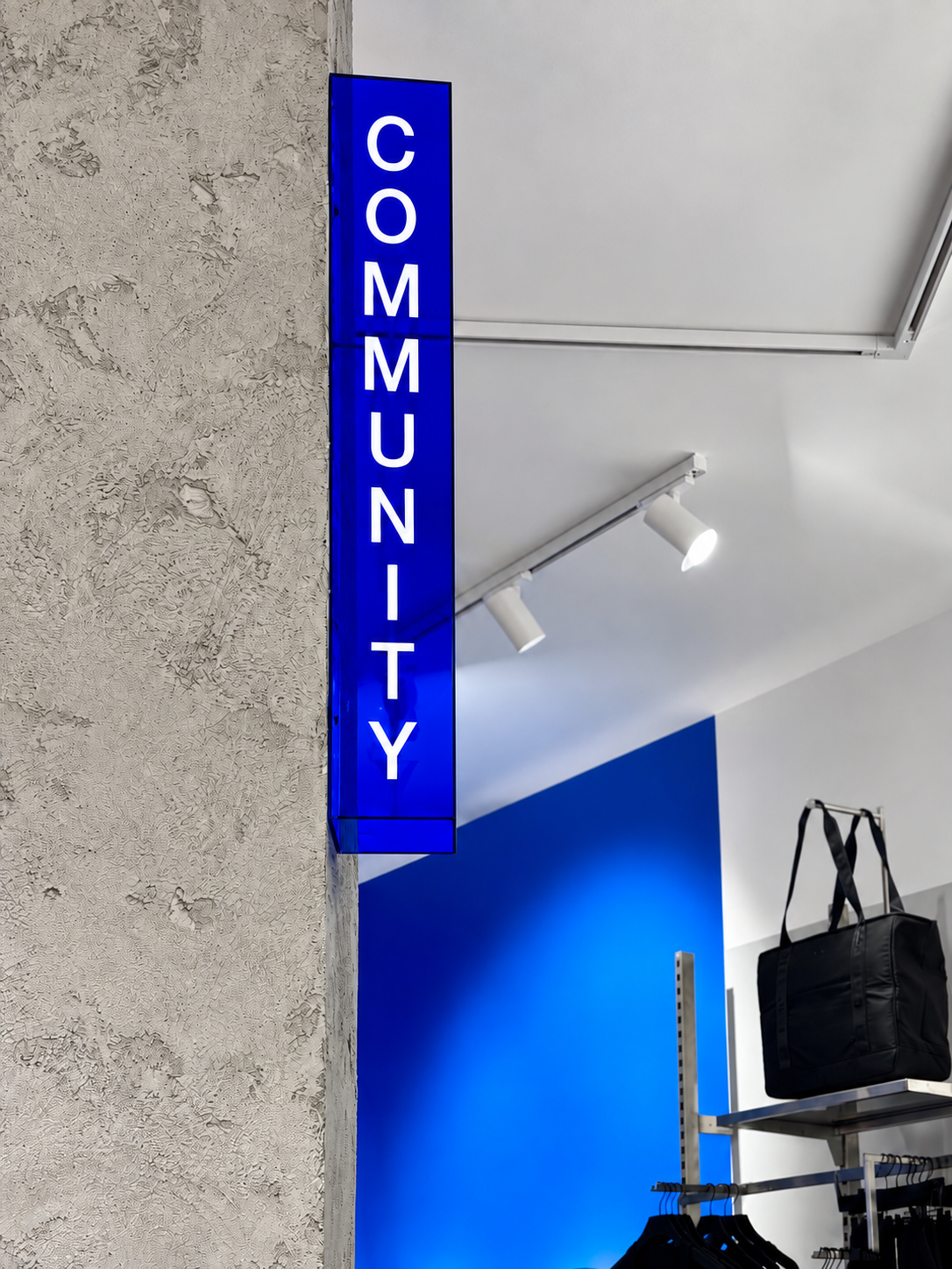 Cobalt blue illuminated Community sign against a textured concrete column.