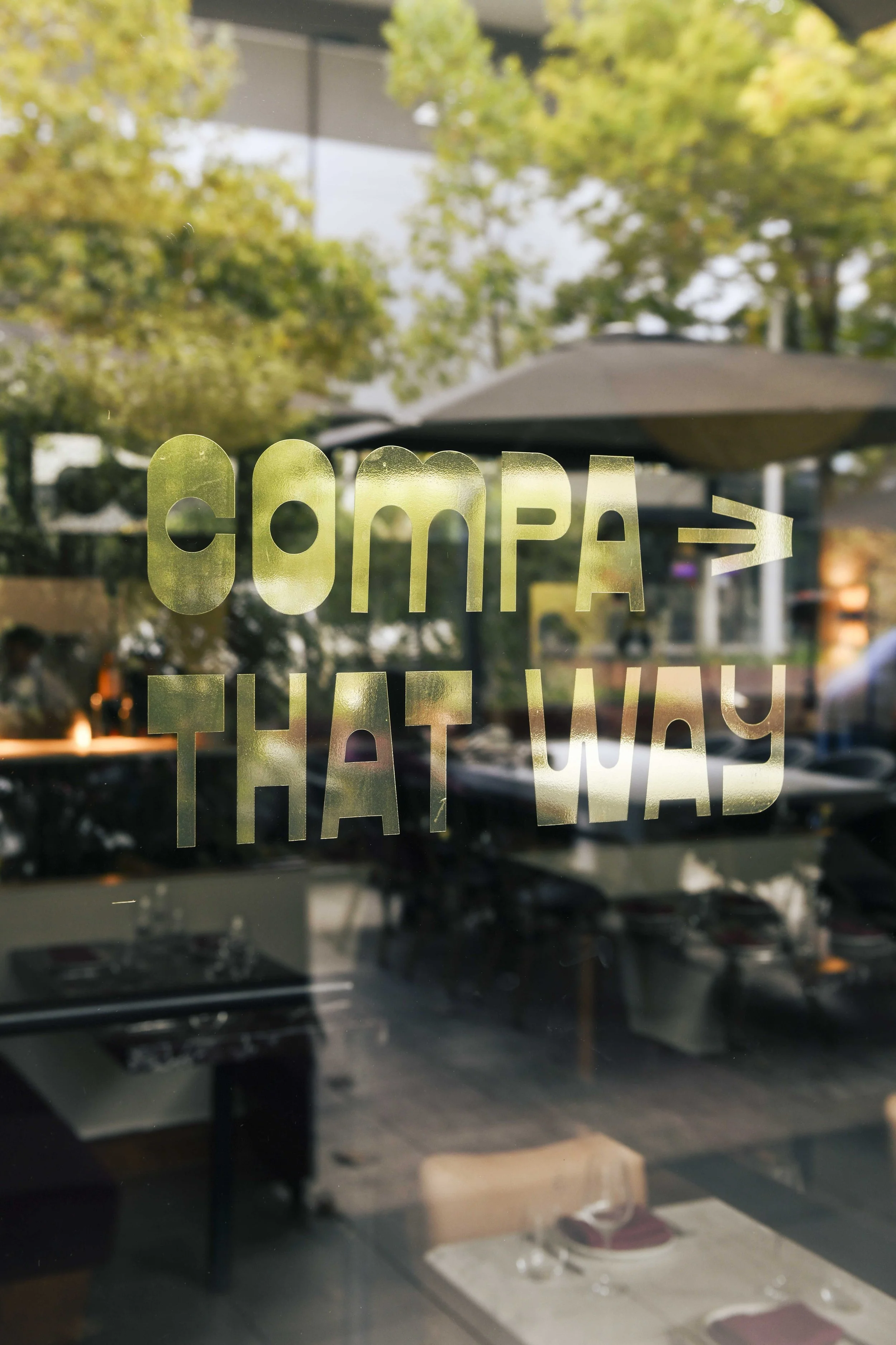 A window decal with the words 'Connect That Way' and an arrow pointing to the right, reflected in the glass are trees, umbrellas, and tables outside a restaurant or café.