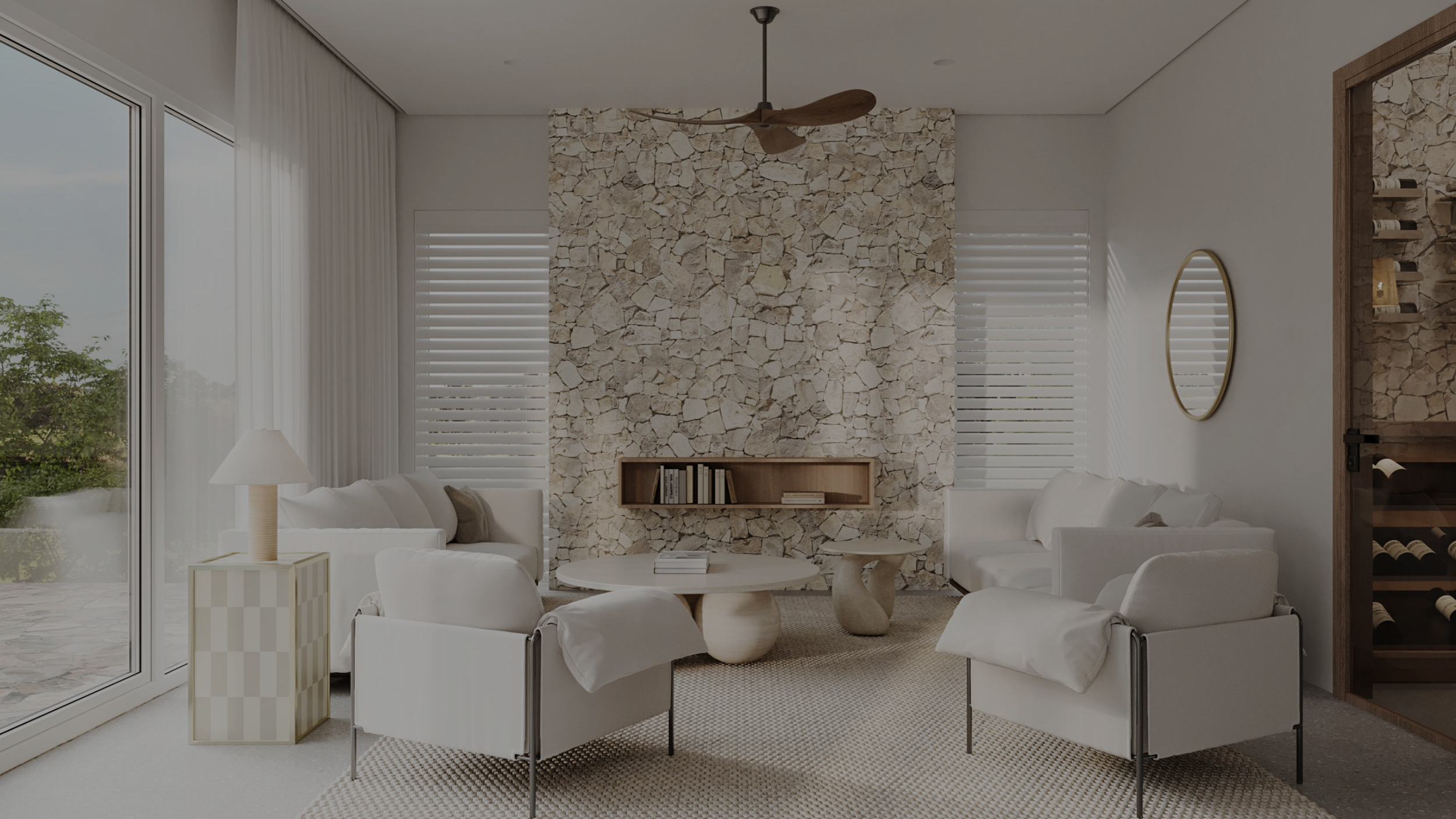 Living room with white furniture, stone fireplace wall, round coffee table with books, side table with lamp, round mirror, wine storage on the right, large window with greenery outside.