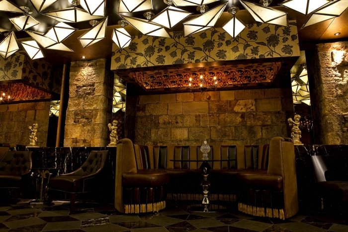 A dimly lit lounge area with leather booths, stone walls, and geometric ceiling lights.