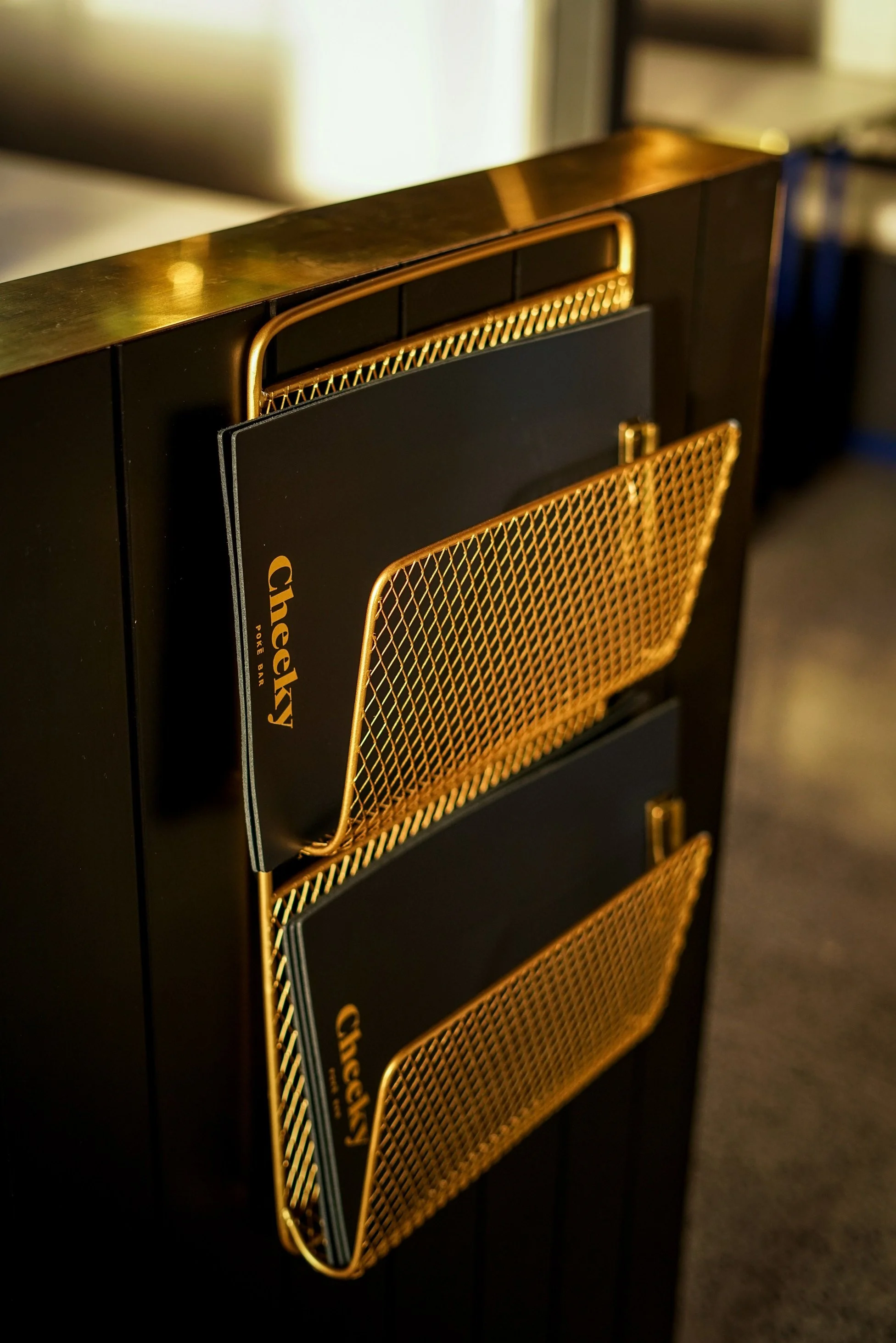 Black menu holders with gold mesh pockets on a black bar or counter.