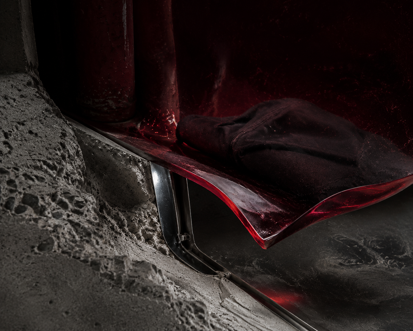 A red chair with a black hoodie placed on its seat, situated next to a rough, textured concrete wall.