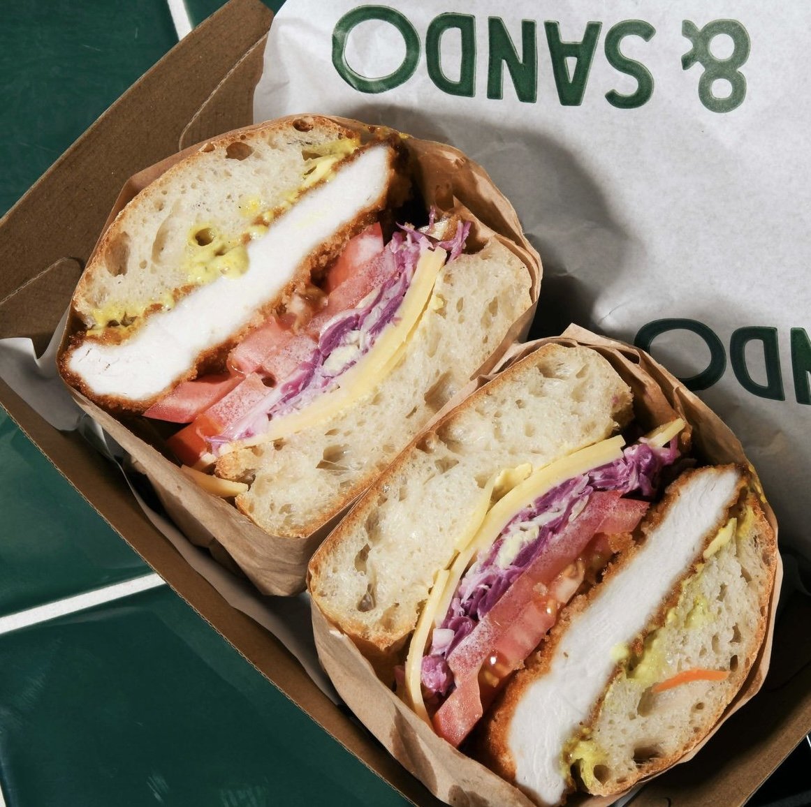 Sandwich with chicken, cheese, tomato, and cabbage in a cardboard box.