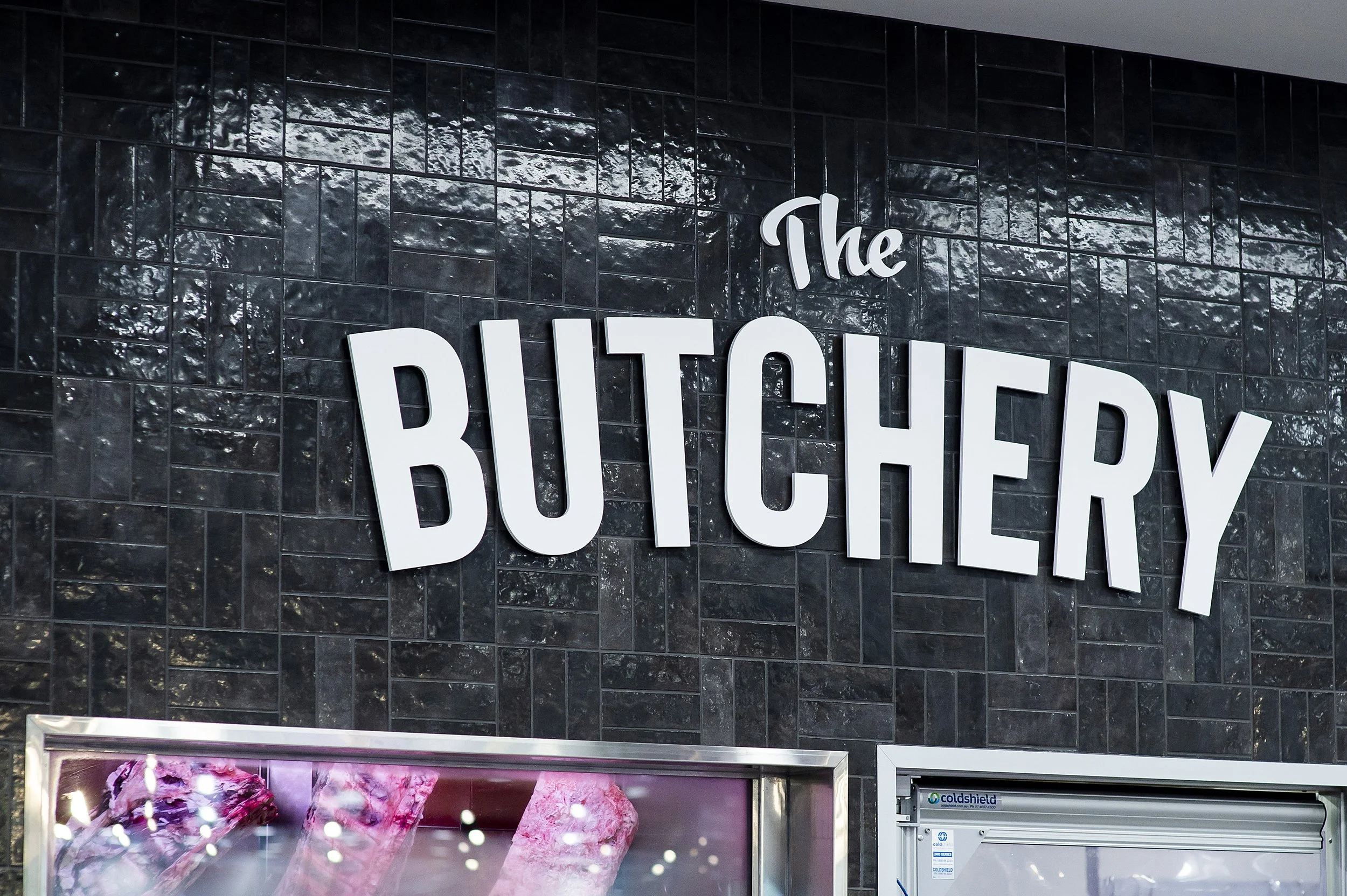 Sign reading 'The Butchery' on a black tiled wall outside a butcher shop.