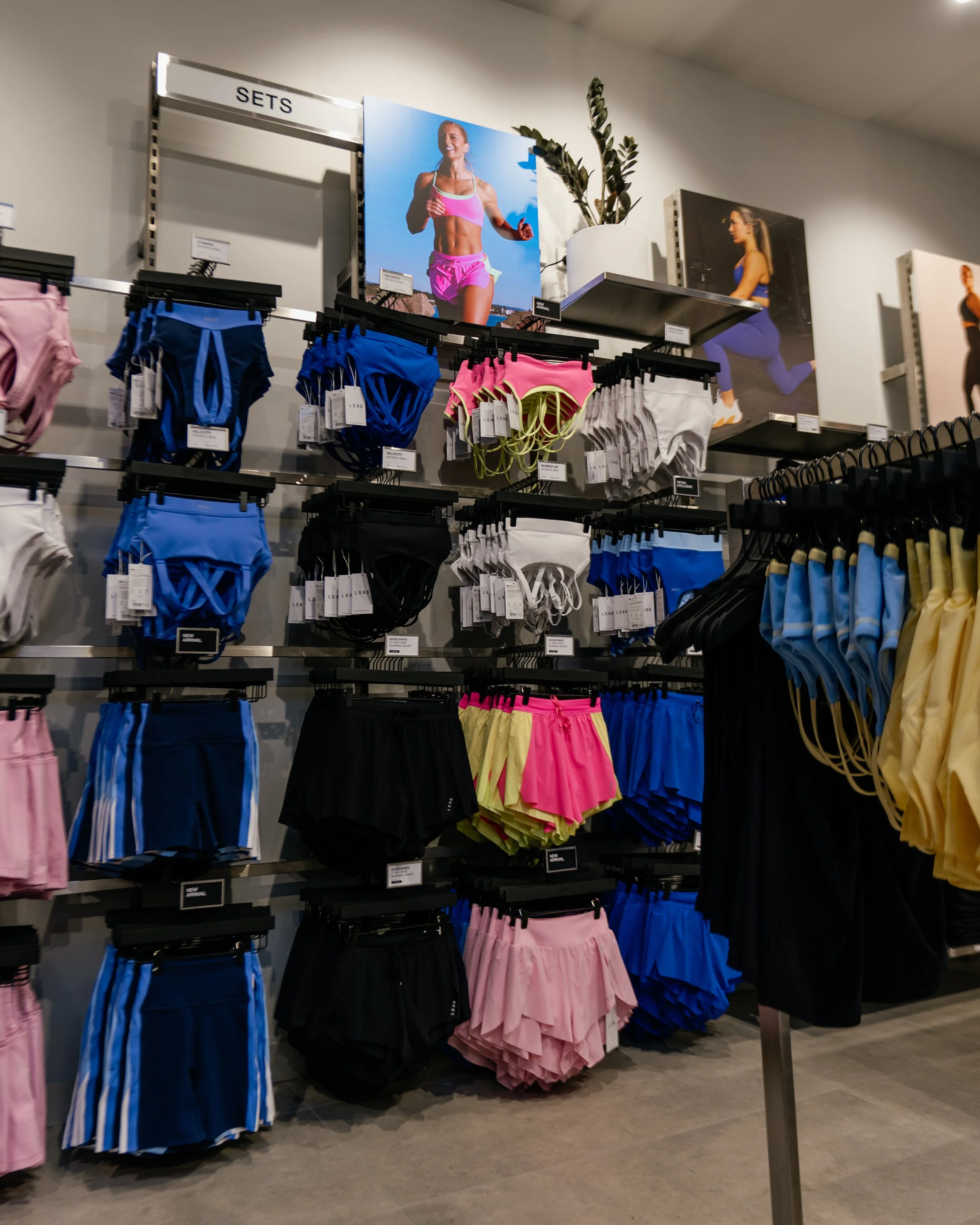 LSKD Karrinyup activewear wall with metal display fixtures, colourful apparel and a campaign screen.