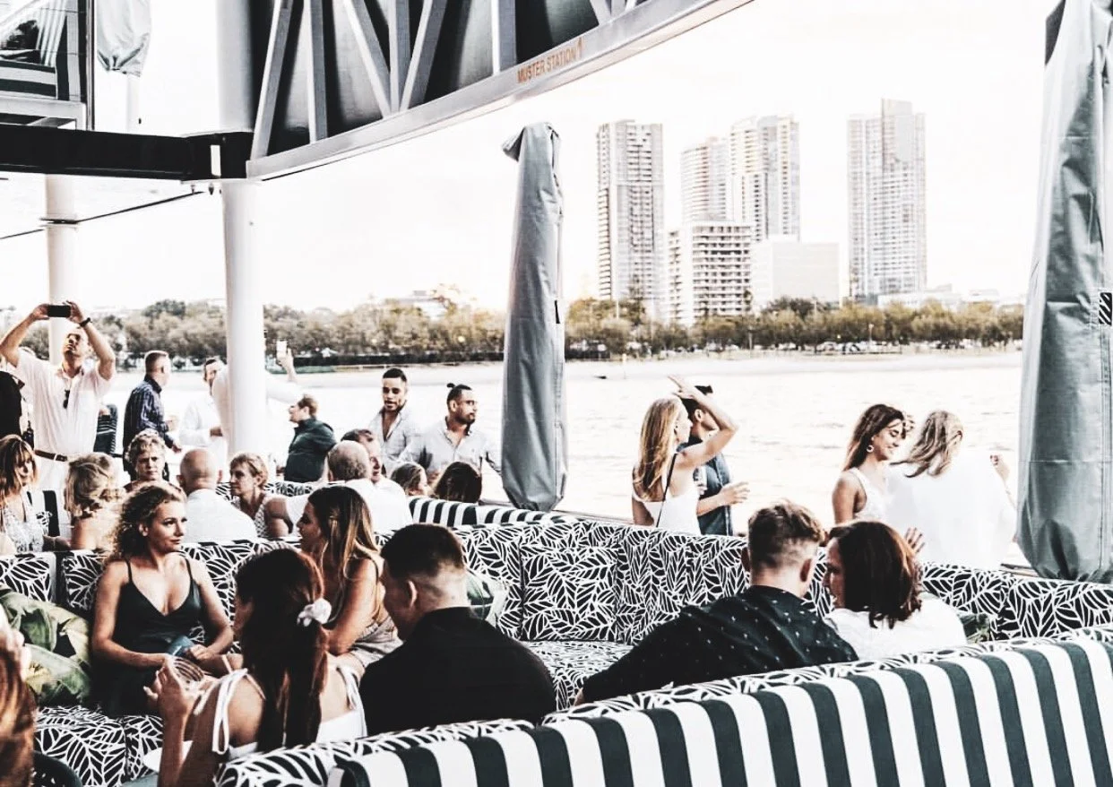 People on a boat or ferry enjoying a gathering by the water with city buildings in the background.