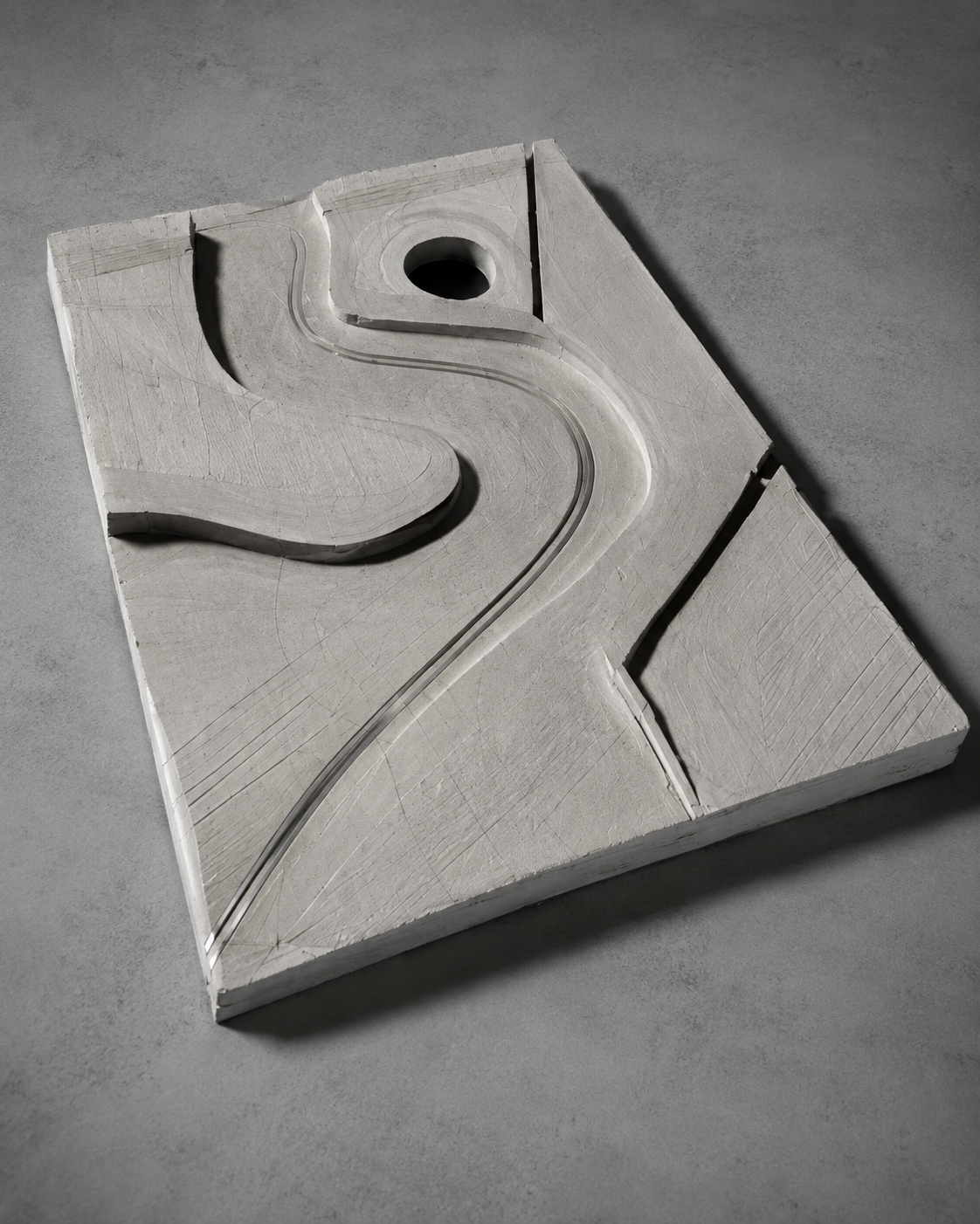 A white sculpture of the letter 'S' with a curved road design carved into it, mounted on a square block with a round hole at the top.