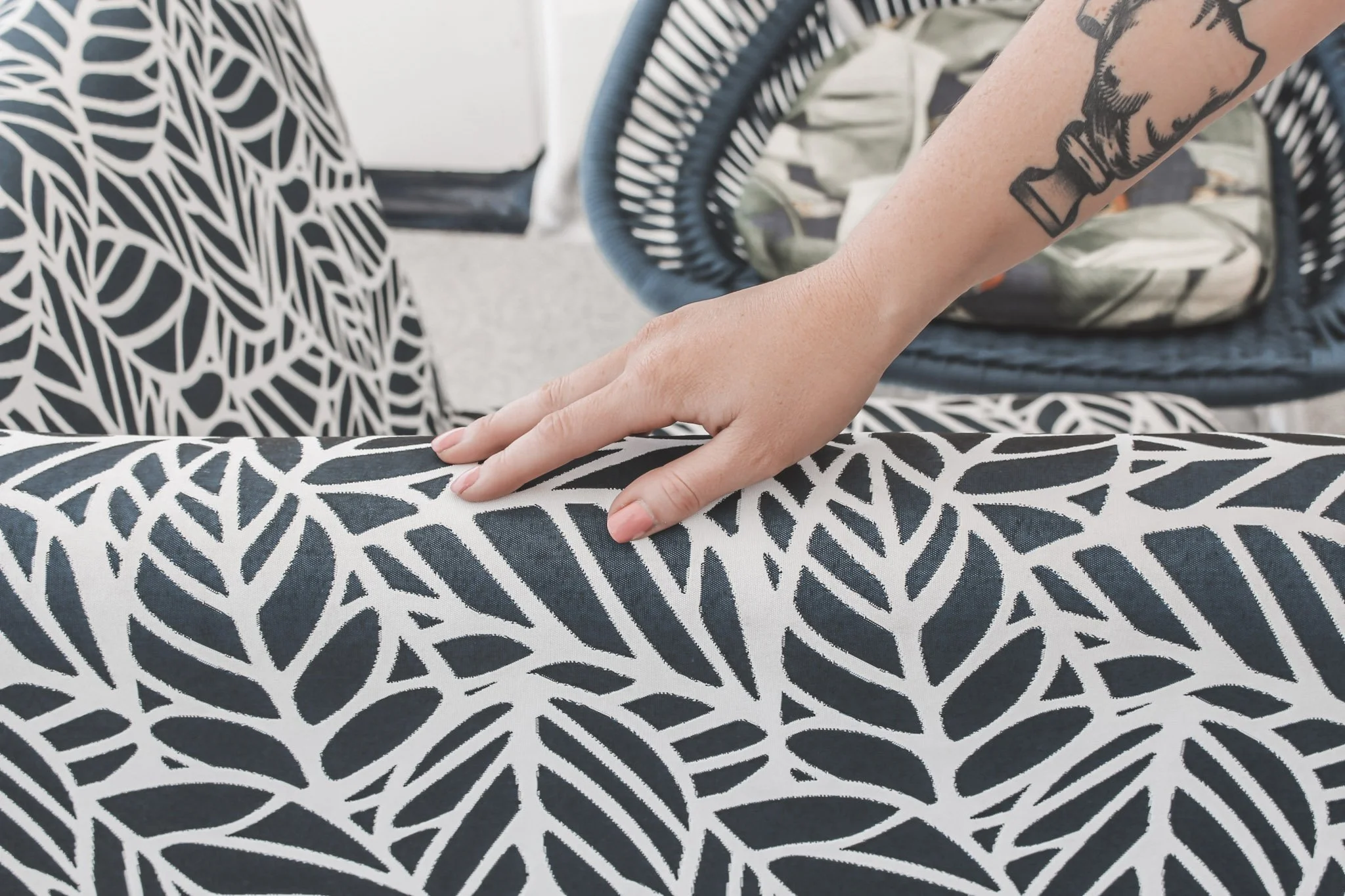 Person with tattoo on arm touching a fabric with a black and white leaf pattern.