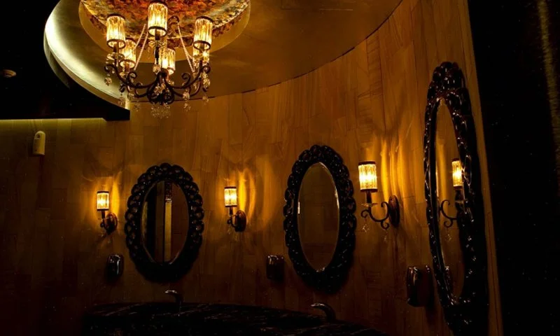 Luxurious interior with a chandelier, wall-mounted lights, circular mirrors, and wooden wall paneling.