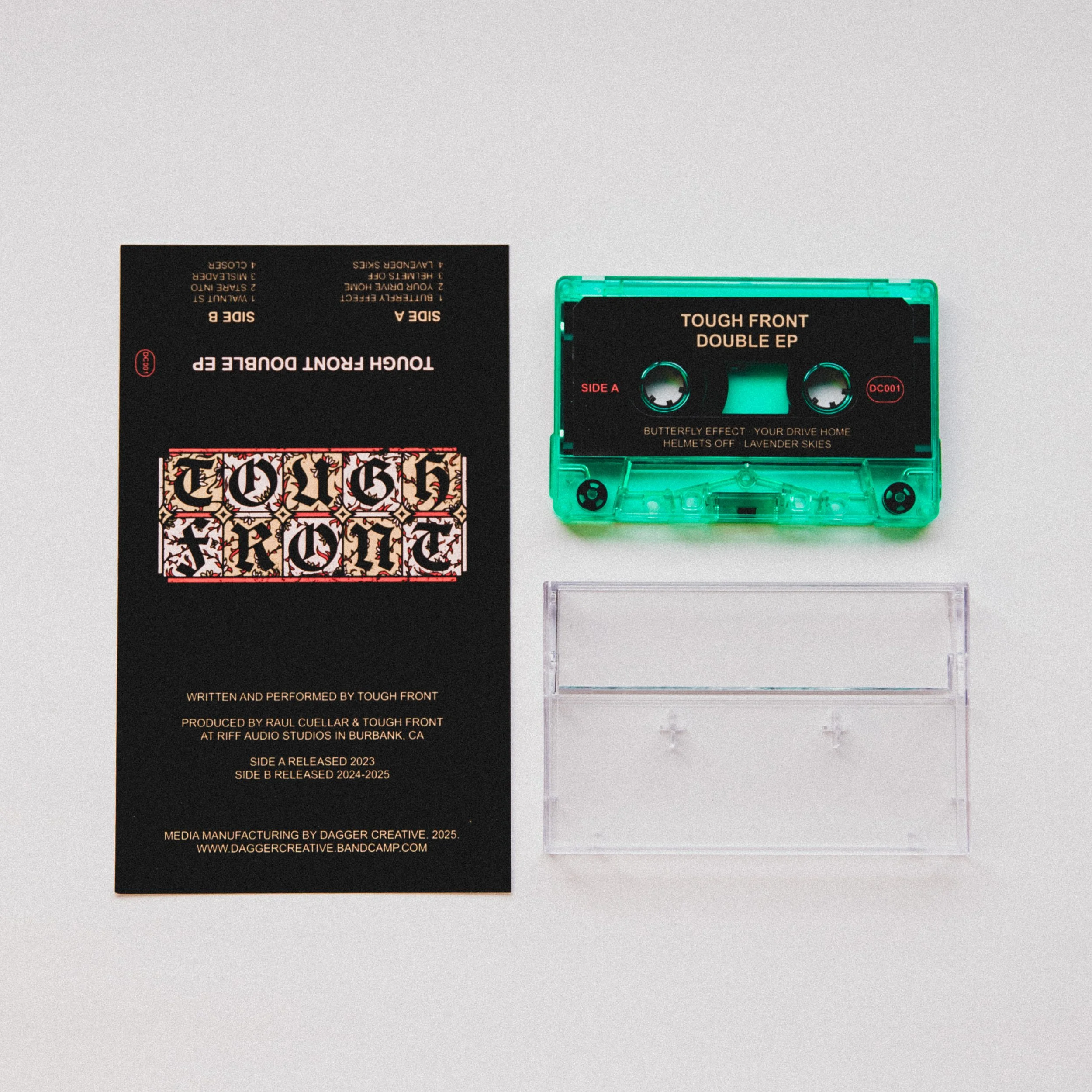 A black cassette tape case with clear plastic cover, a green cassette tape with black label, and a black paper insert with text and a decorative logo.