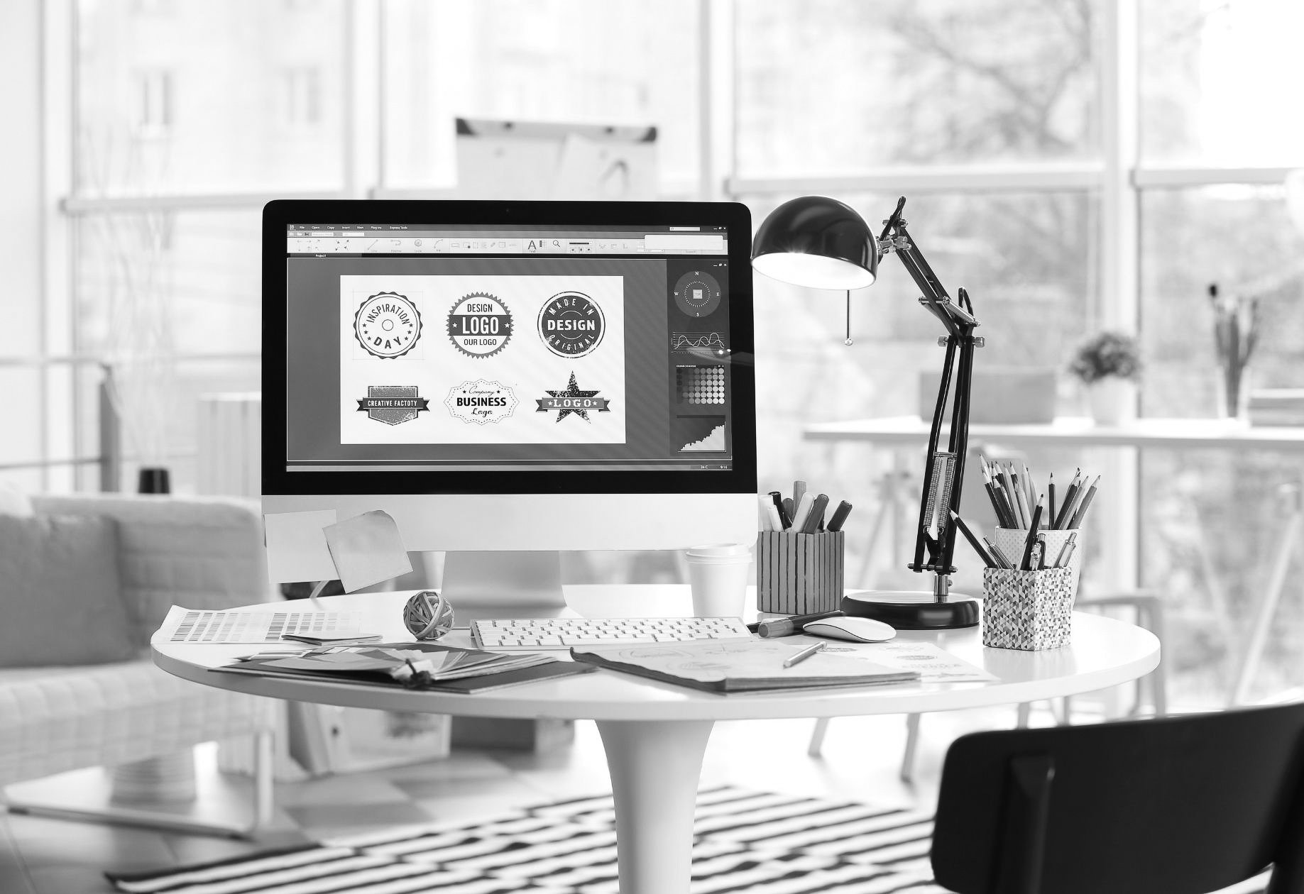Een bureau met kleurstalen en een computerscherm met logo-ontwerpen.