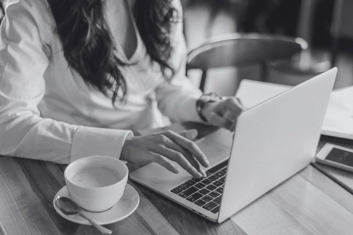Een vrouw werkt aan een laptop, met een leeg theekopje ernaast.